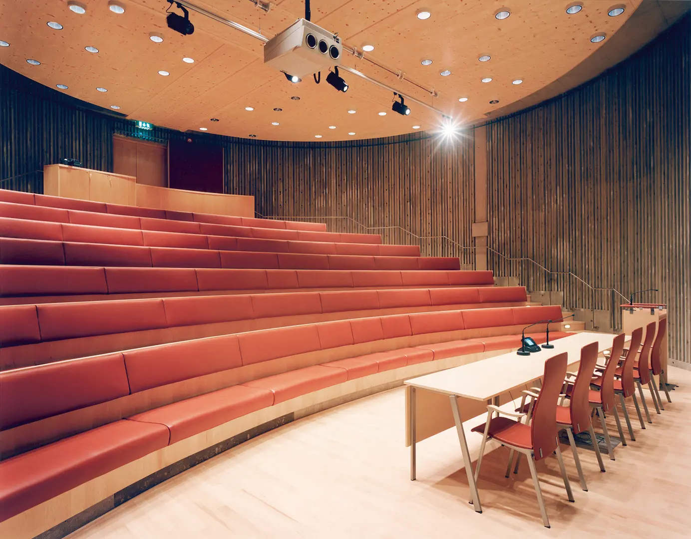 Hörsal med långa bänkrader med röd klädsel.