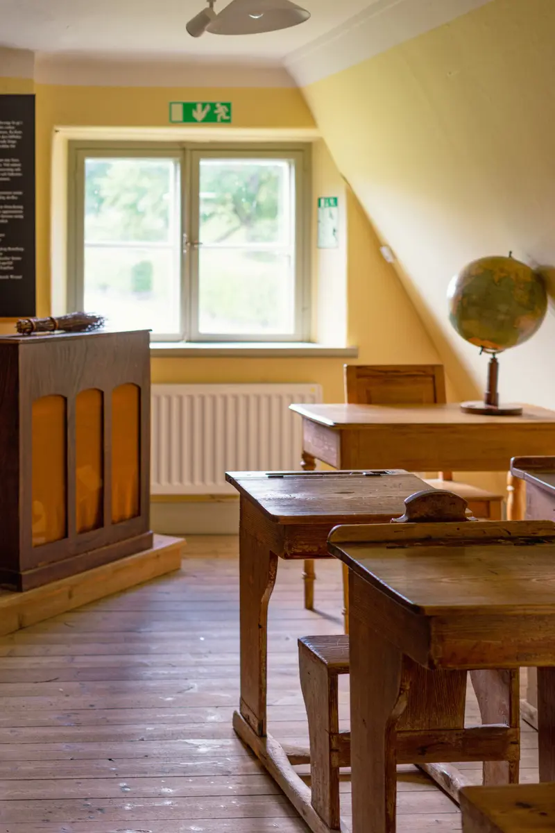 Skolmiljö: en kateder med ett risknippe på, små bänkar i barnstorlek och en jordglob.