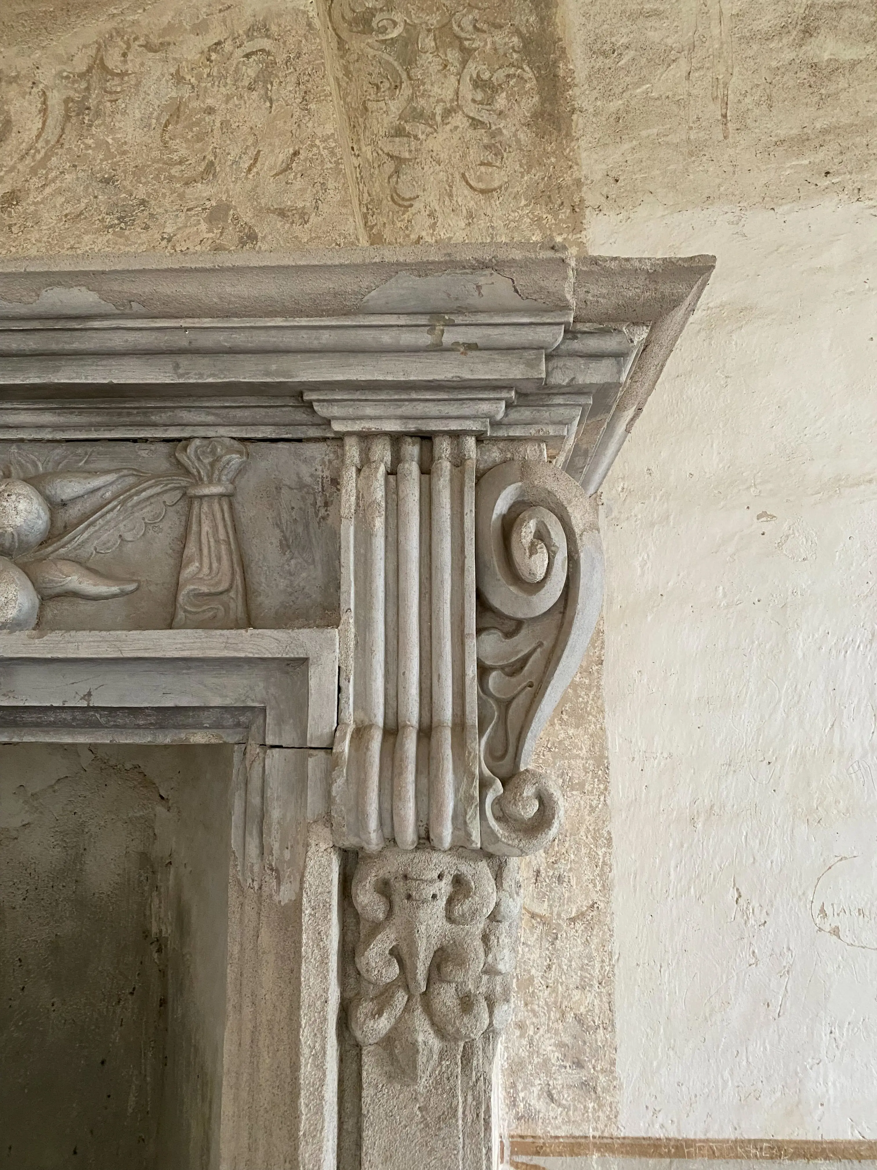 Interiör närbild på en huggen spisomfattning. På väggen anas rester av målningar.