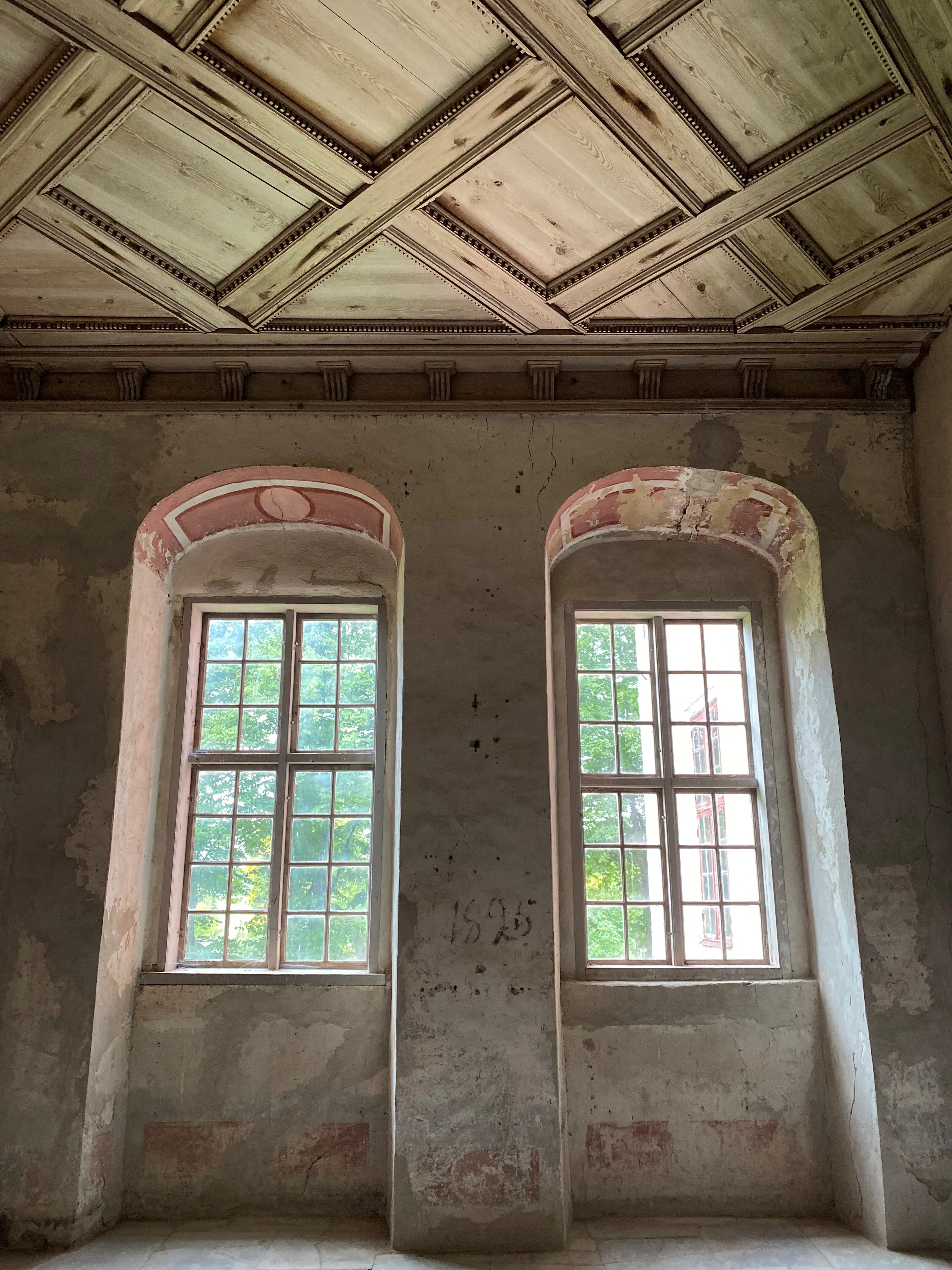 Interiörbild som visar två ganla fönster med omålade träbågar och många rutor. Målningar förnsteröppningarnas övre rundning samt omålat kassettak. Putsade väggar.