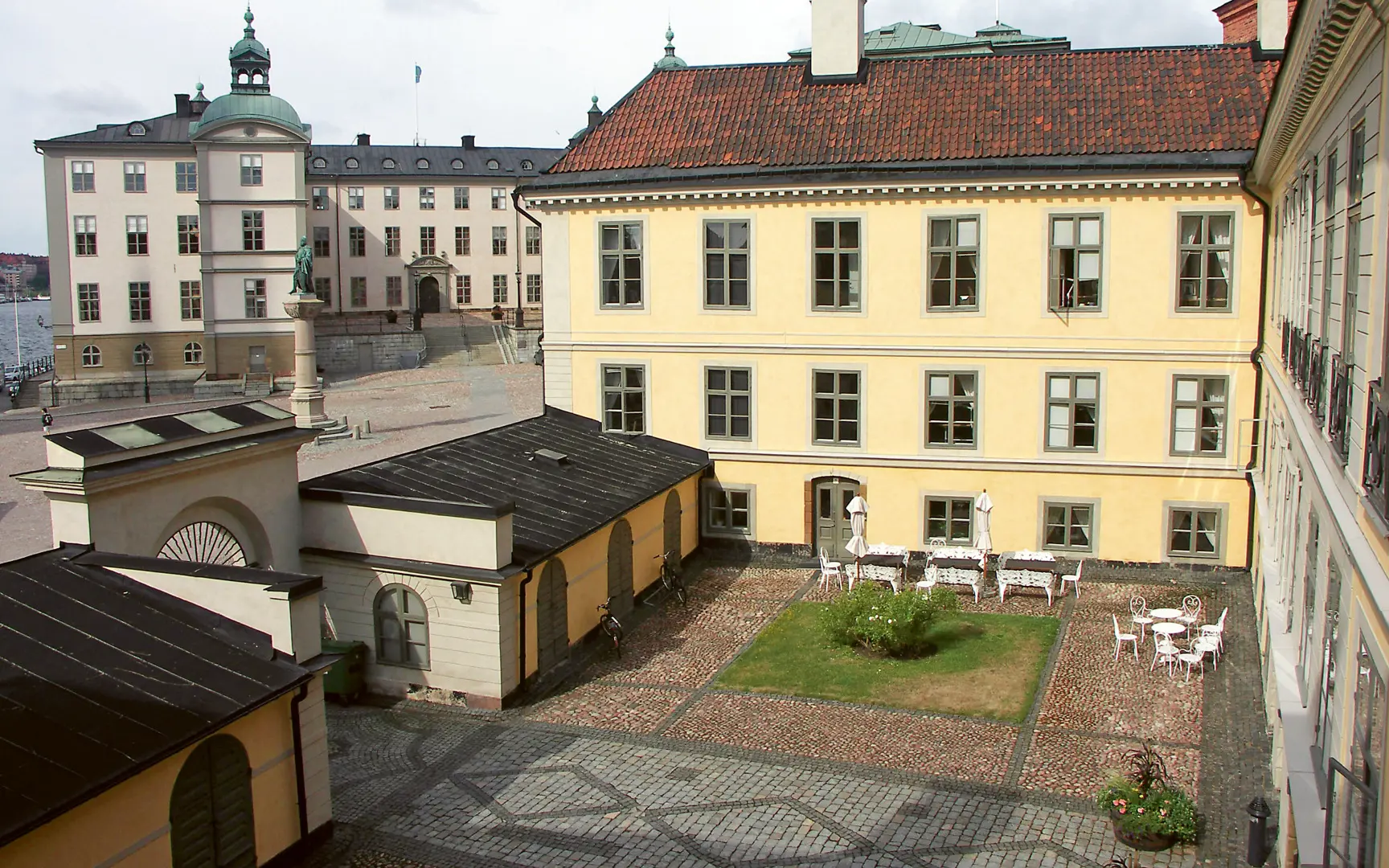 Hessensteinska husets innergård mellan de gulputsade flyglarna. På gården har kullersten lagts i mönster, och i ett hörn står några vita trädgårdsmöbler.