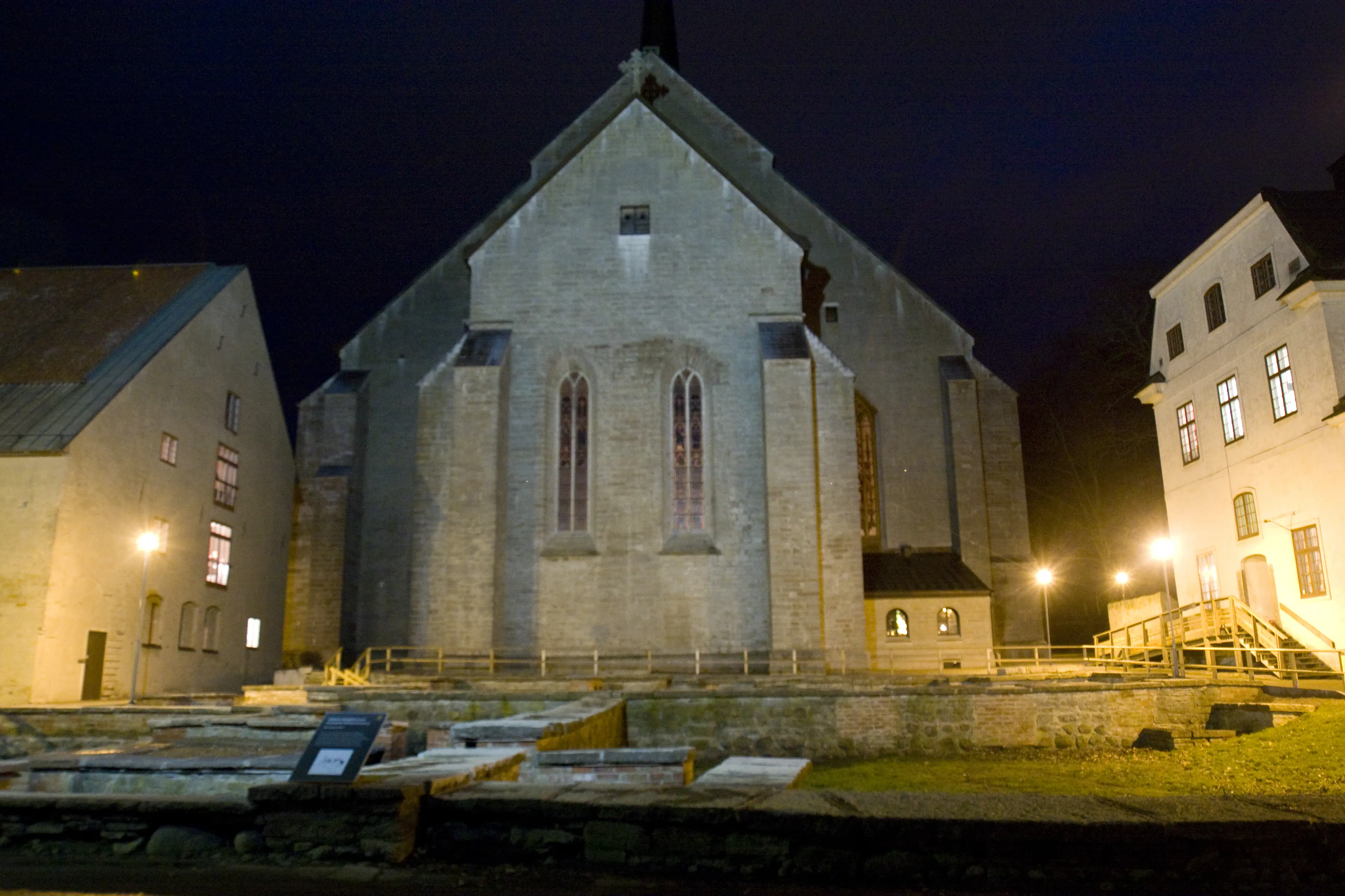 Vadstena kloster. Kyrkan och ruinparken. Till vänster i bild syns gaveln på en av nunneklostrets byggnader, till höger gaveln på munkklostret. Kväll.
