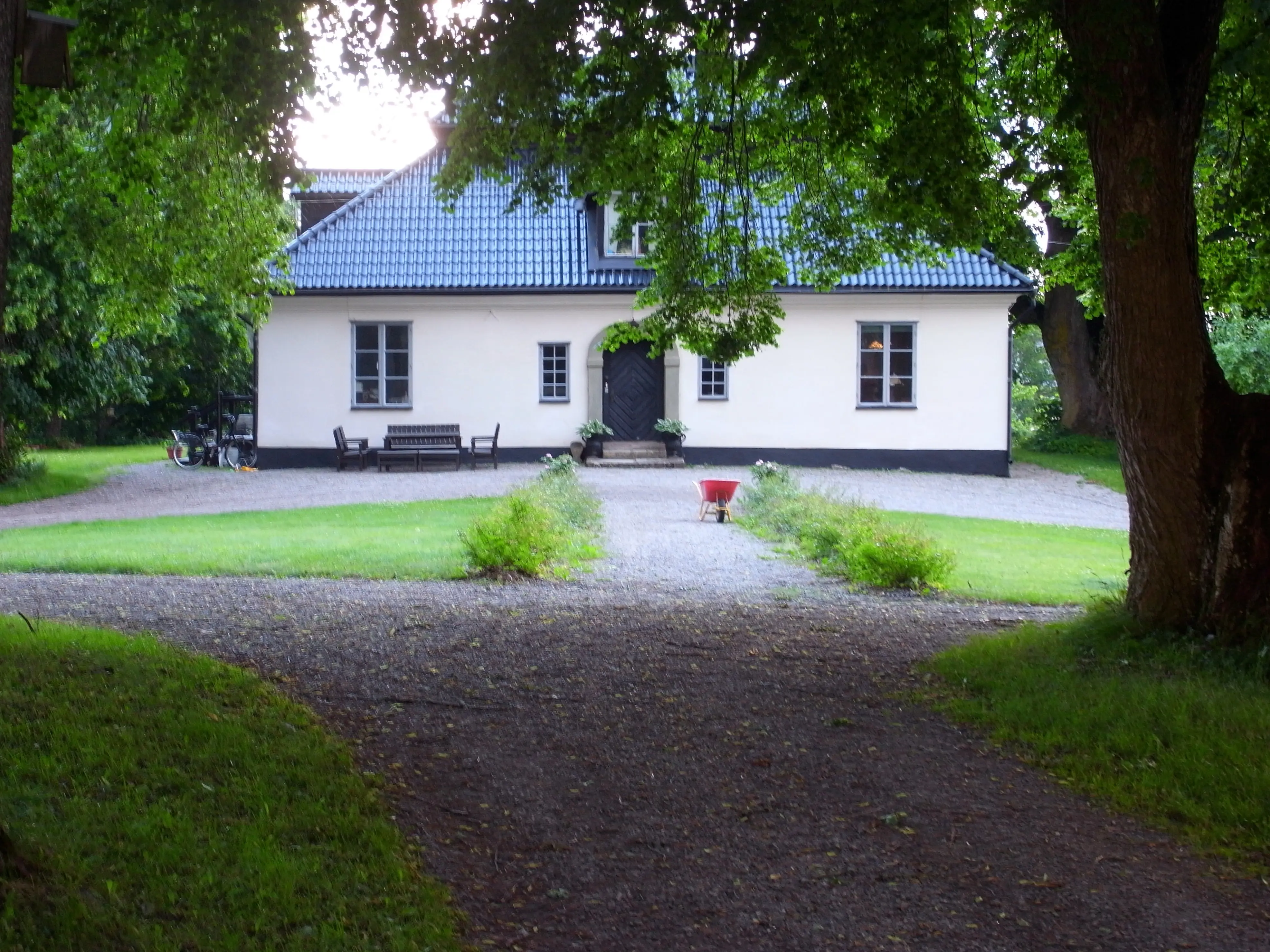 Mangårdsbyggnaden på Ådö. En vitputsad byggnad med brant, valmat tak och tak-kupa. Sommar och grönska.