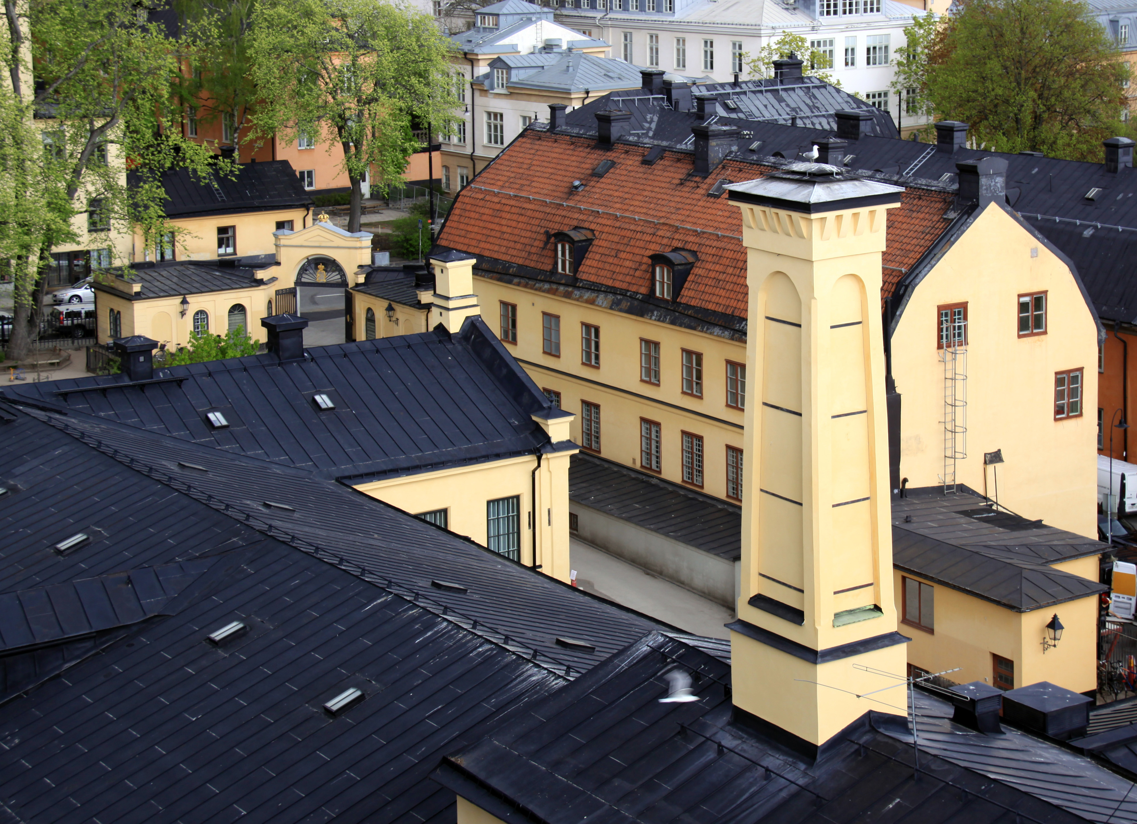 Kungliga Myntet sett från ovan. I förgrunden verkstadshusets svarta plåt-tak och höga skorsten. Vår och grönska.