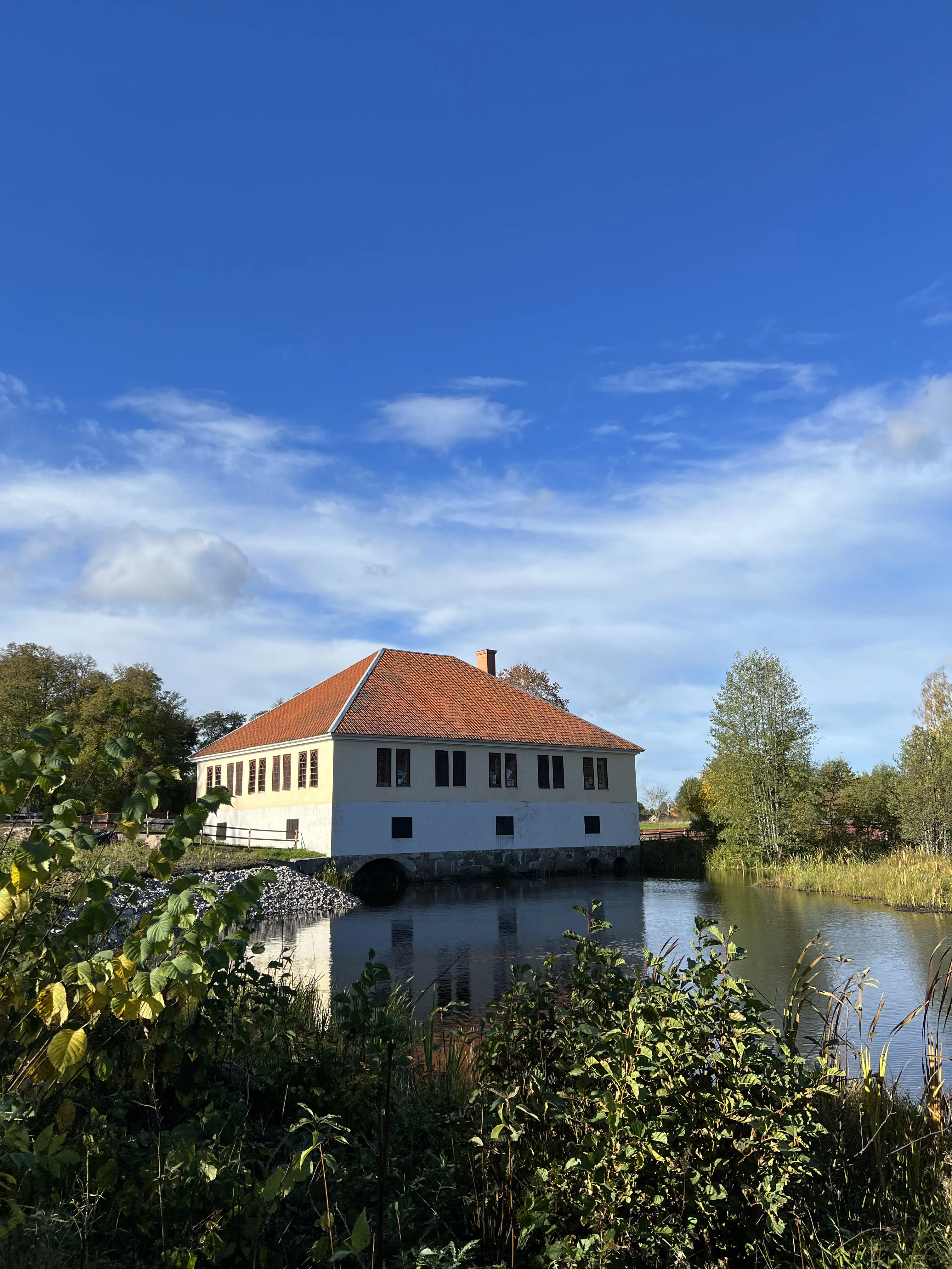 Övre dammen vid Lövstabruk. En stor stenbyggnad med valmat tak. Genom ett valv i byggnadens källare rinner vatten som samlas i en bred å.