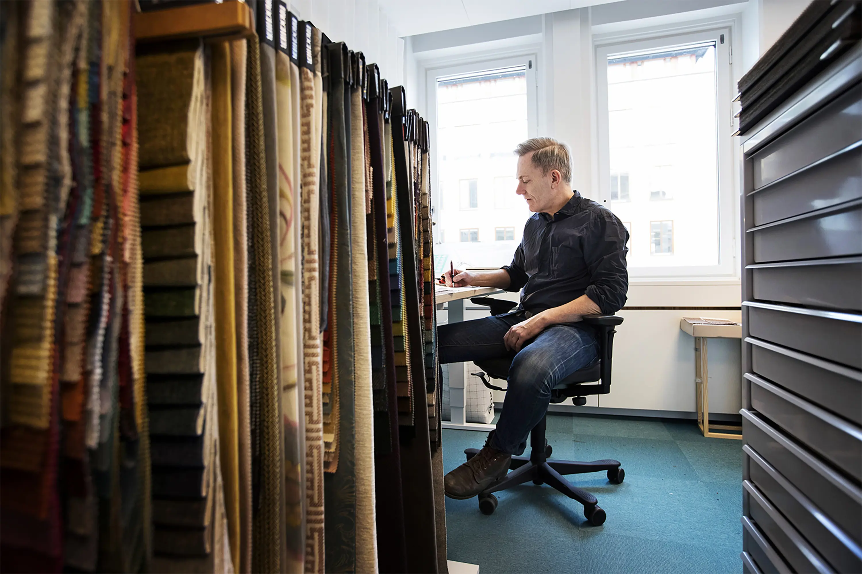 Ulf Agnér vid sitt skrivbord med tygprover i förgrunden.