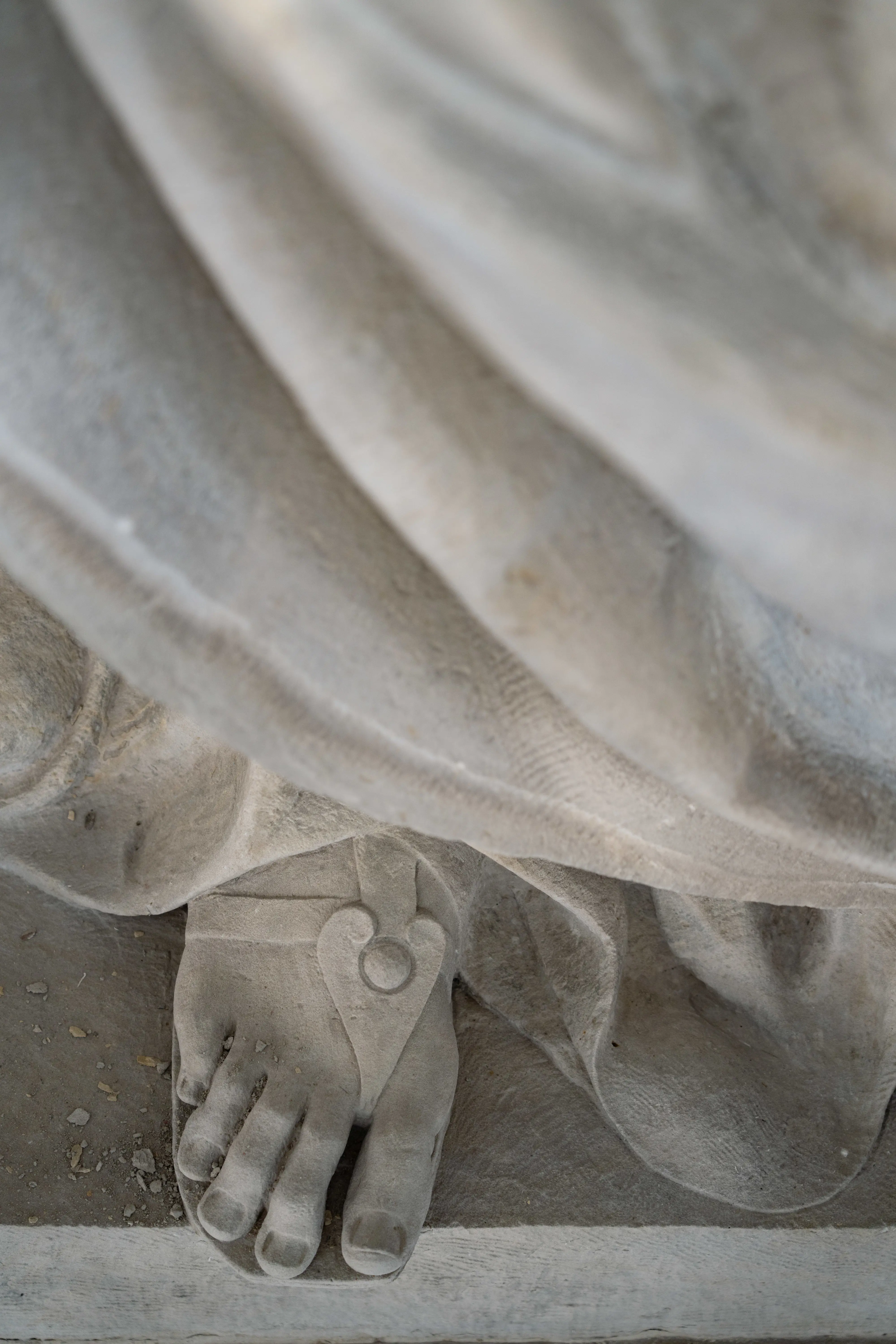 Detalj av stenskulptur. Nedanför en veckad dräkt syns en fot i en sandal.