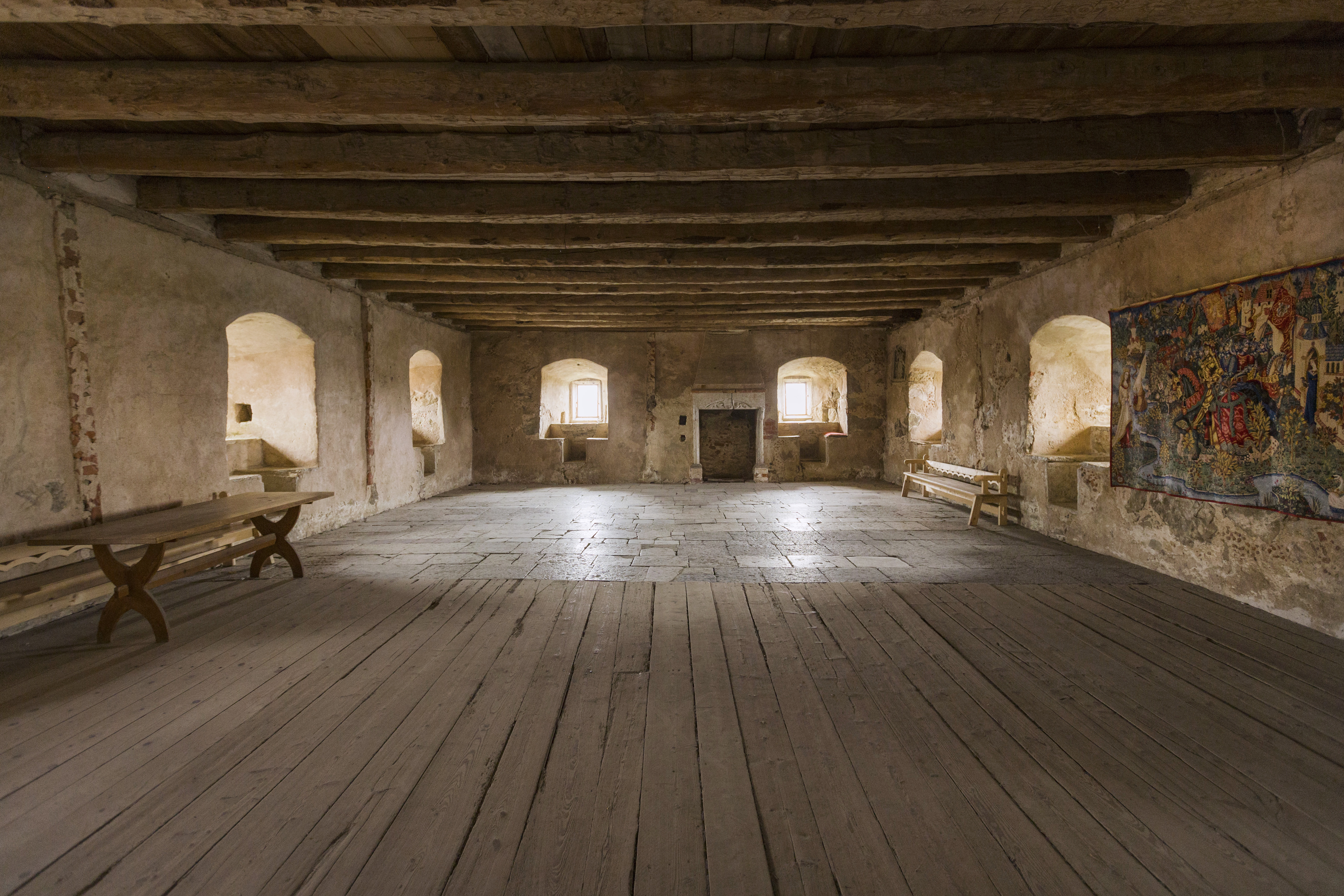 Sal i Glimmingehus. Golvet är av sten och träplank. Taket bärs upp av grova timmer-bjälkar.