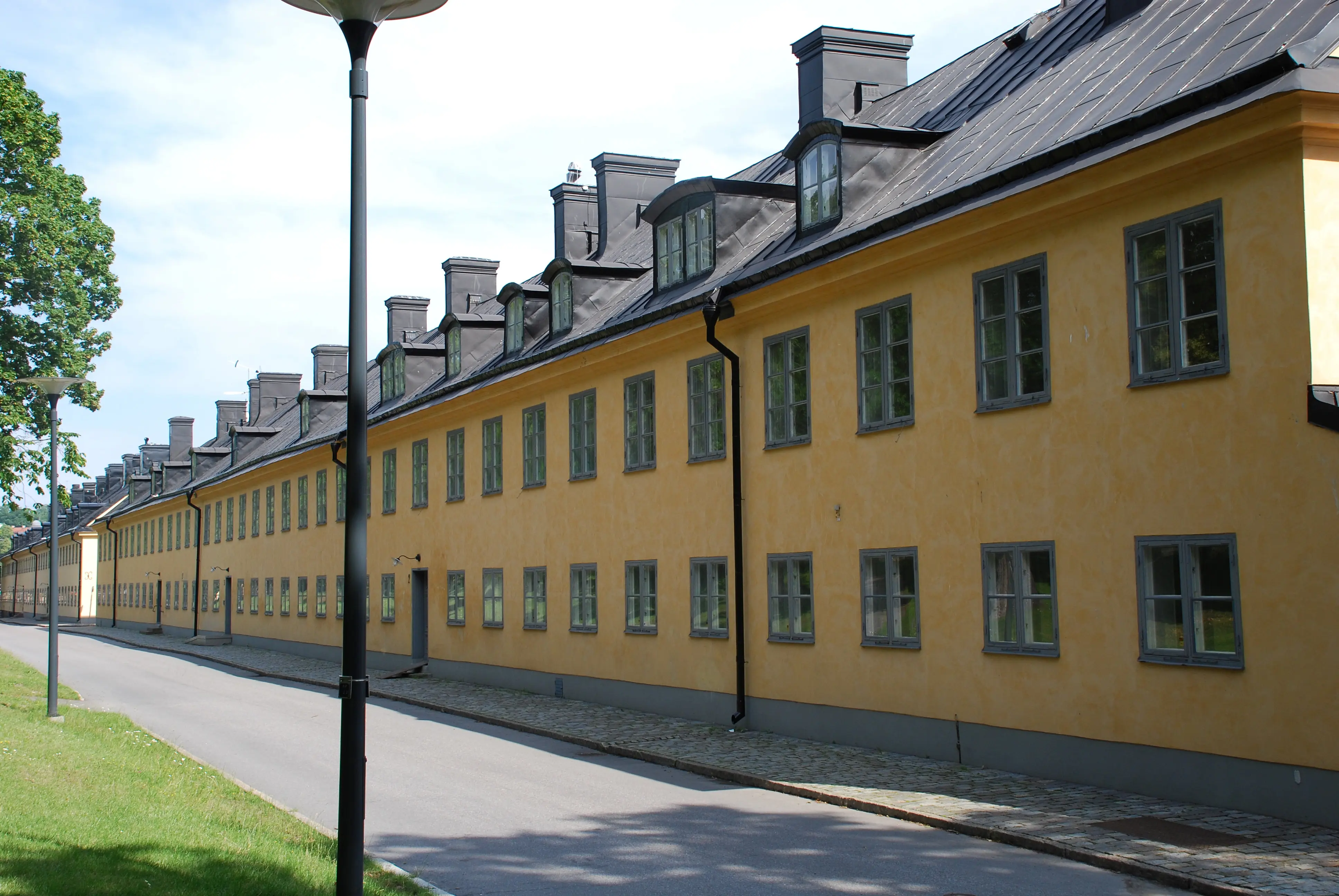Boställshusen på Skeppsholmen. Två långa tvåvångingshus i gul puts. De svarta plåt-taken har tak-kupor.