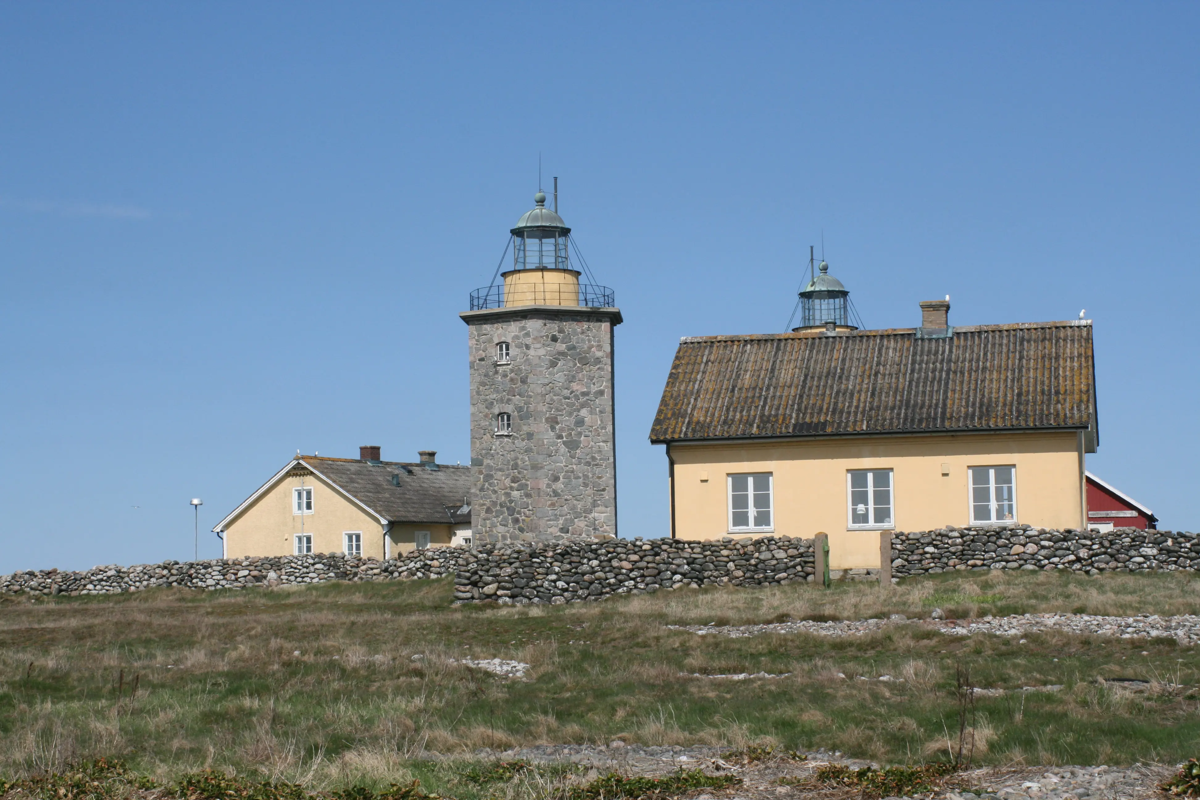 Del av fyrplatsen på Nidingen. Två äldre fyrtorn och omgivande byggnader. Det ena tornet är dolt av ett gult hus, bara lanterninen sticker upp.