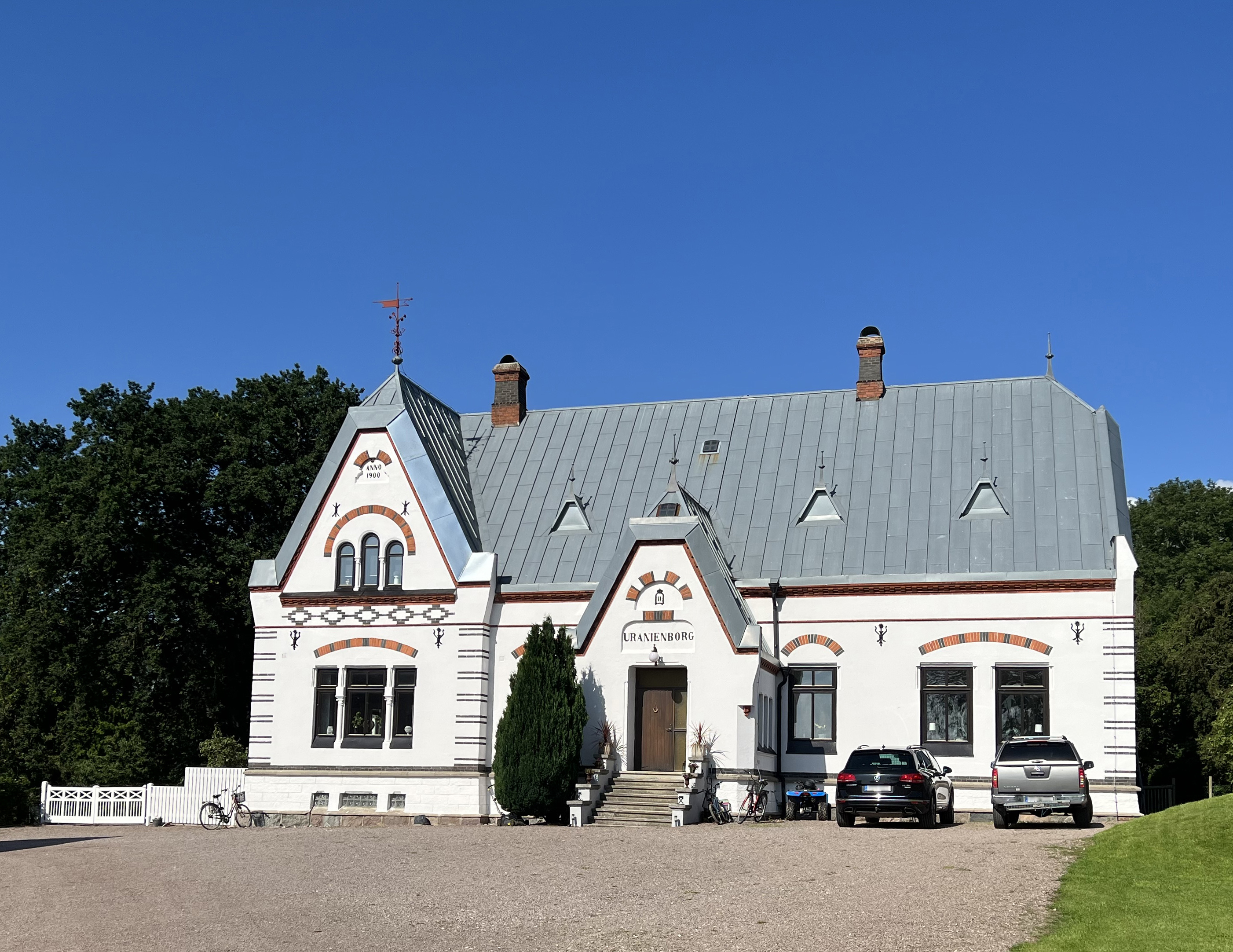 Uranienborg. Vitputsat bostadshus med grått plåt-tak. Fasaden är dekorerad med ankarslut och brunt och svart tegel.