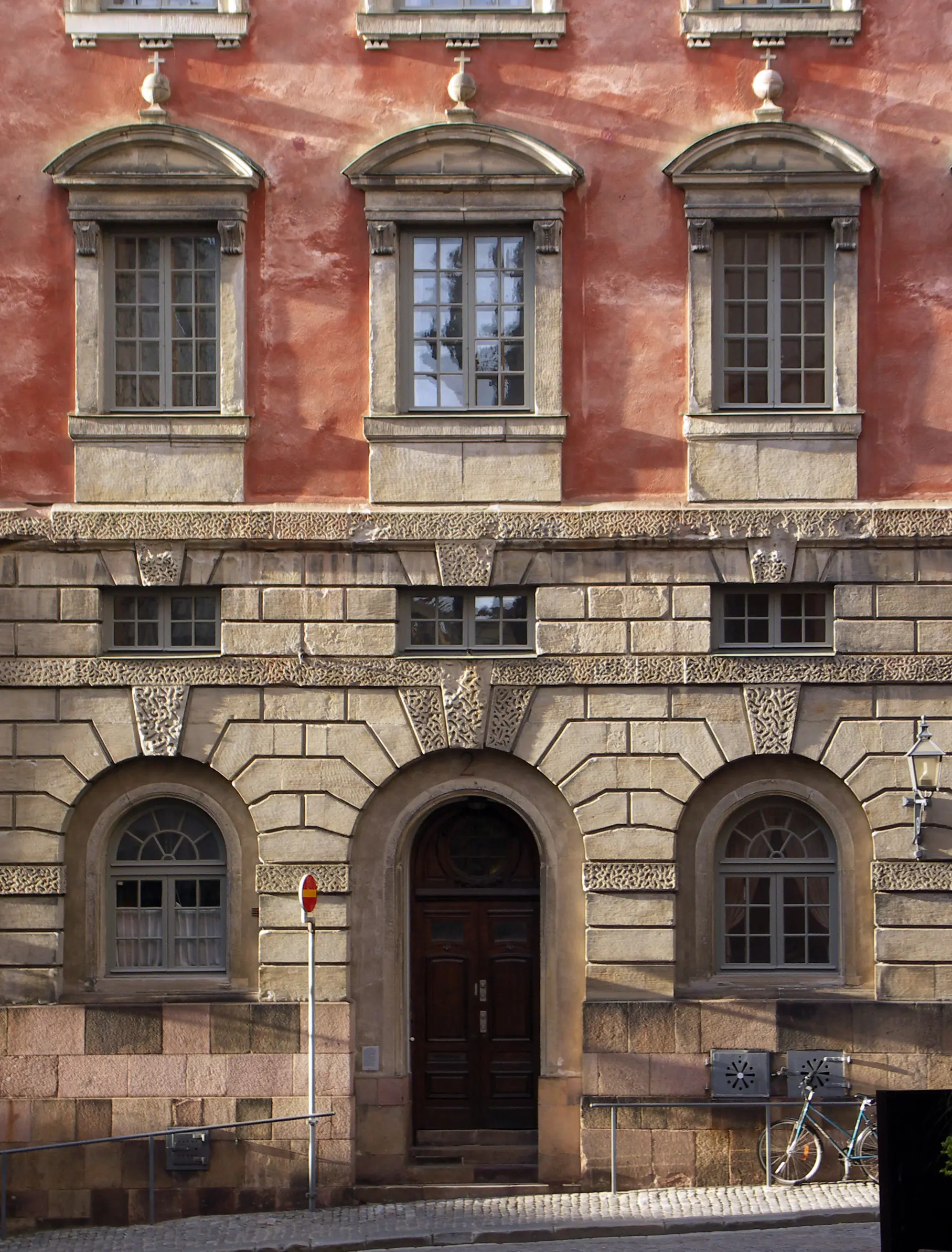 Oxenstiernska palatset. Nedre delen av fasaden är klädd i sten, resten är rödputsad. Porten har ett rundat valv.