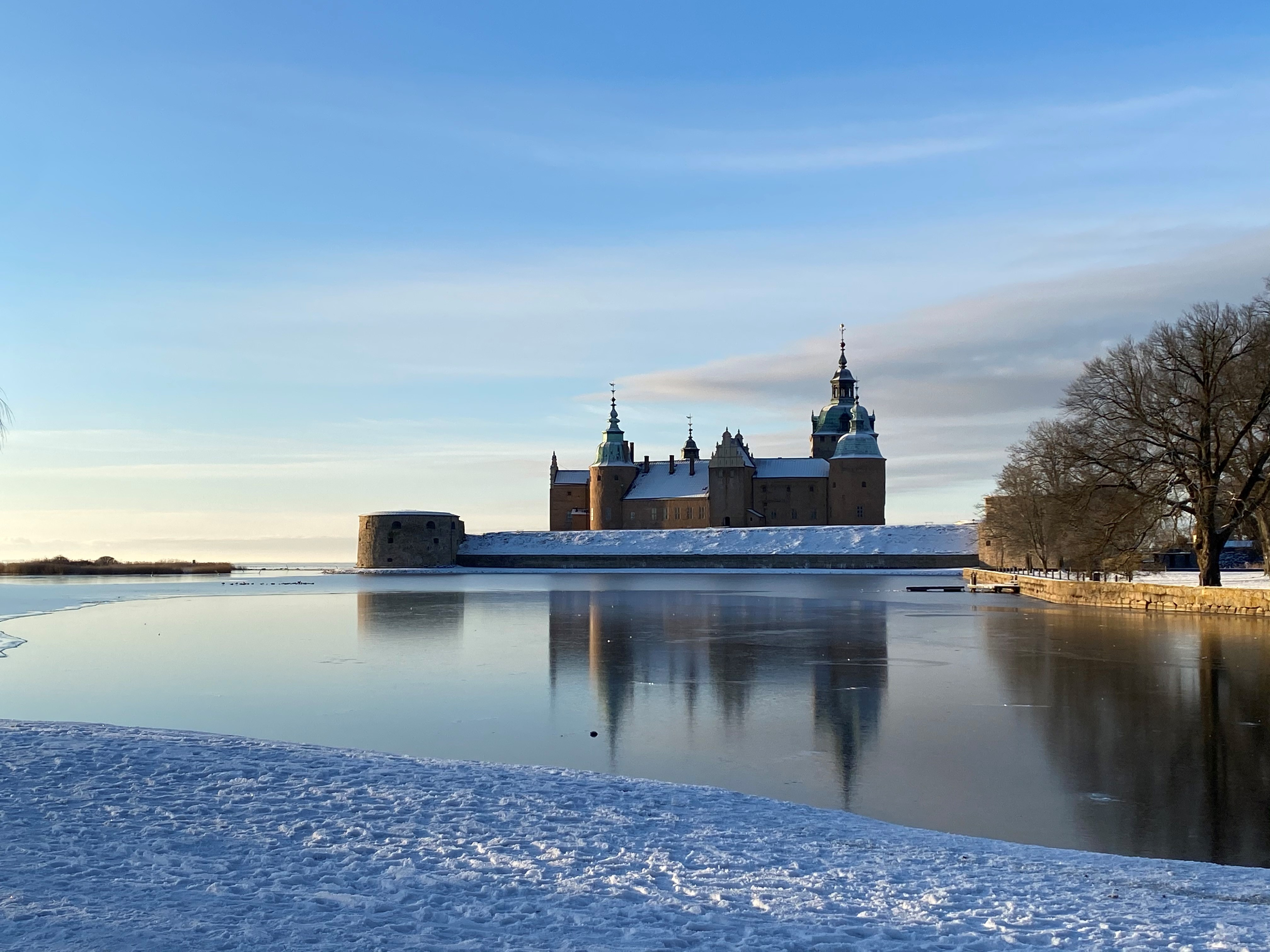 Kalmar slott en solig vinterdag. Snö på marken och is på vattnet intill.