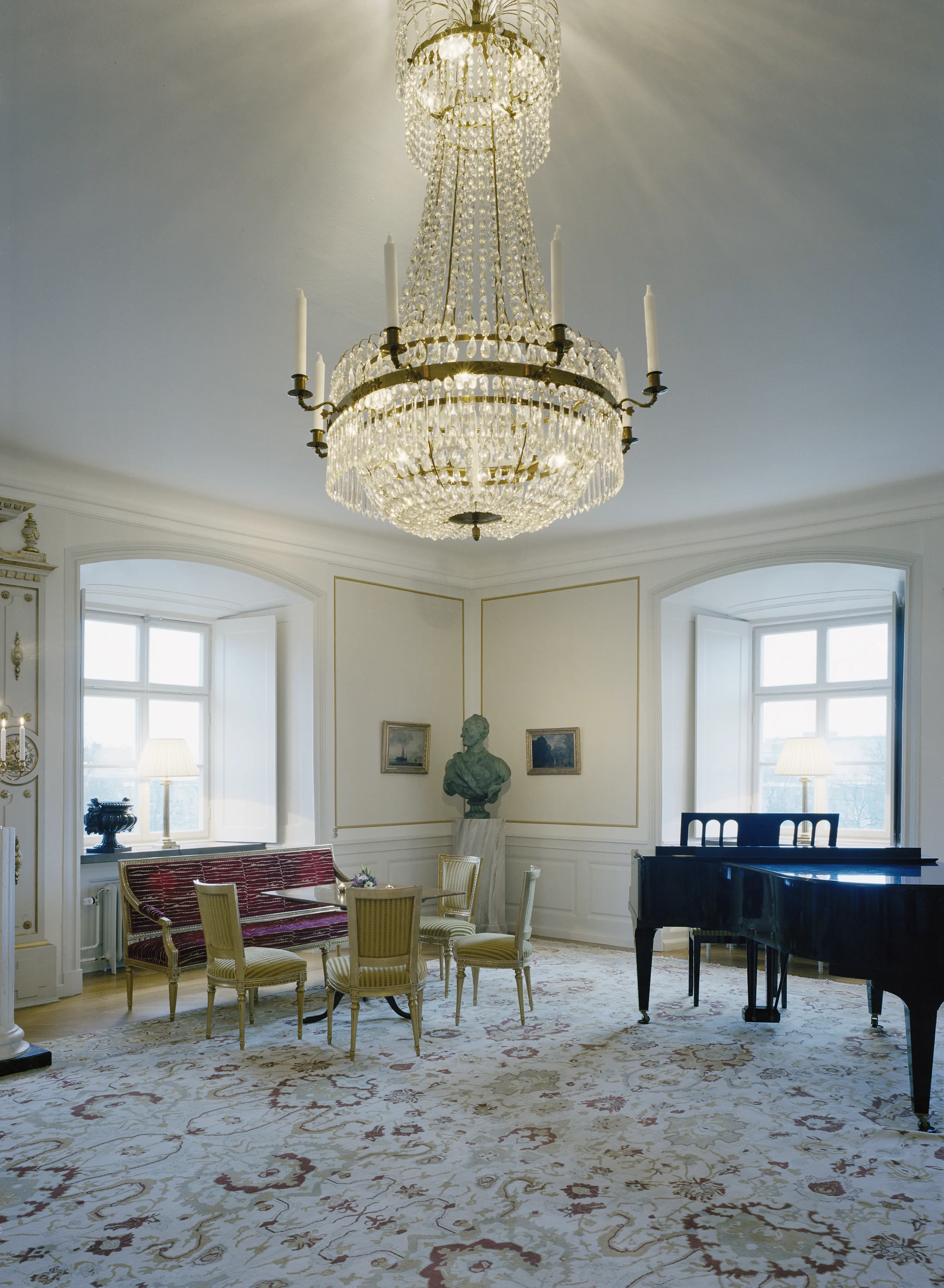 Interiör, Västerås slott. Salong i residenset, inredd i empir-stil. Golvet täcks av en ljus matta med växt-ornamentik. I taket hänger en stor kristall-krona.