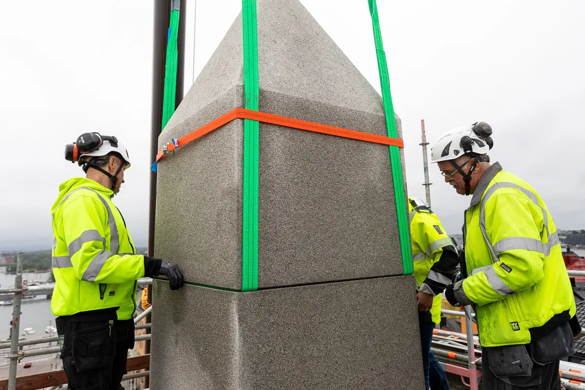 Obelisken på slottsbacken under restaurerings-arbete. Personer i arbetskläder sätter ett av stensegmenten på plats.