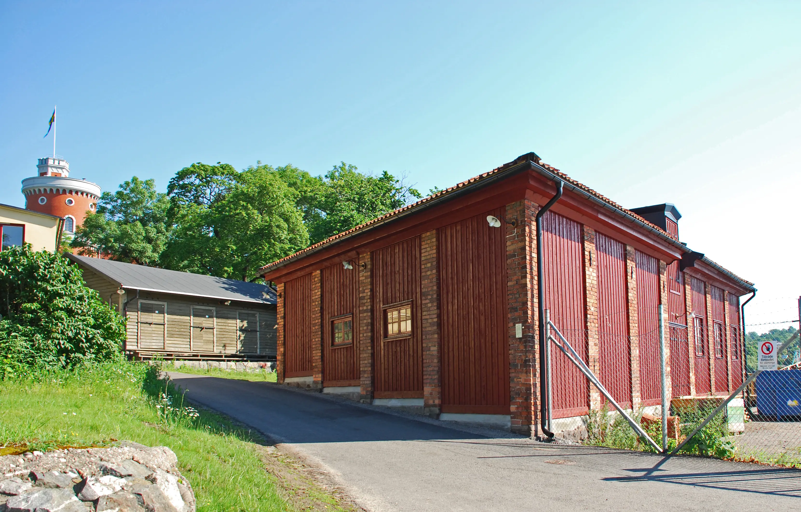 Kolskjulet på Kastellholmen. Fasad i tegel och rödmålat trä. I bakgrunden skymtar kastellet. Sommar och grönska.