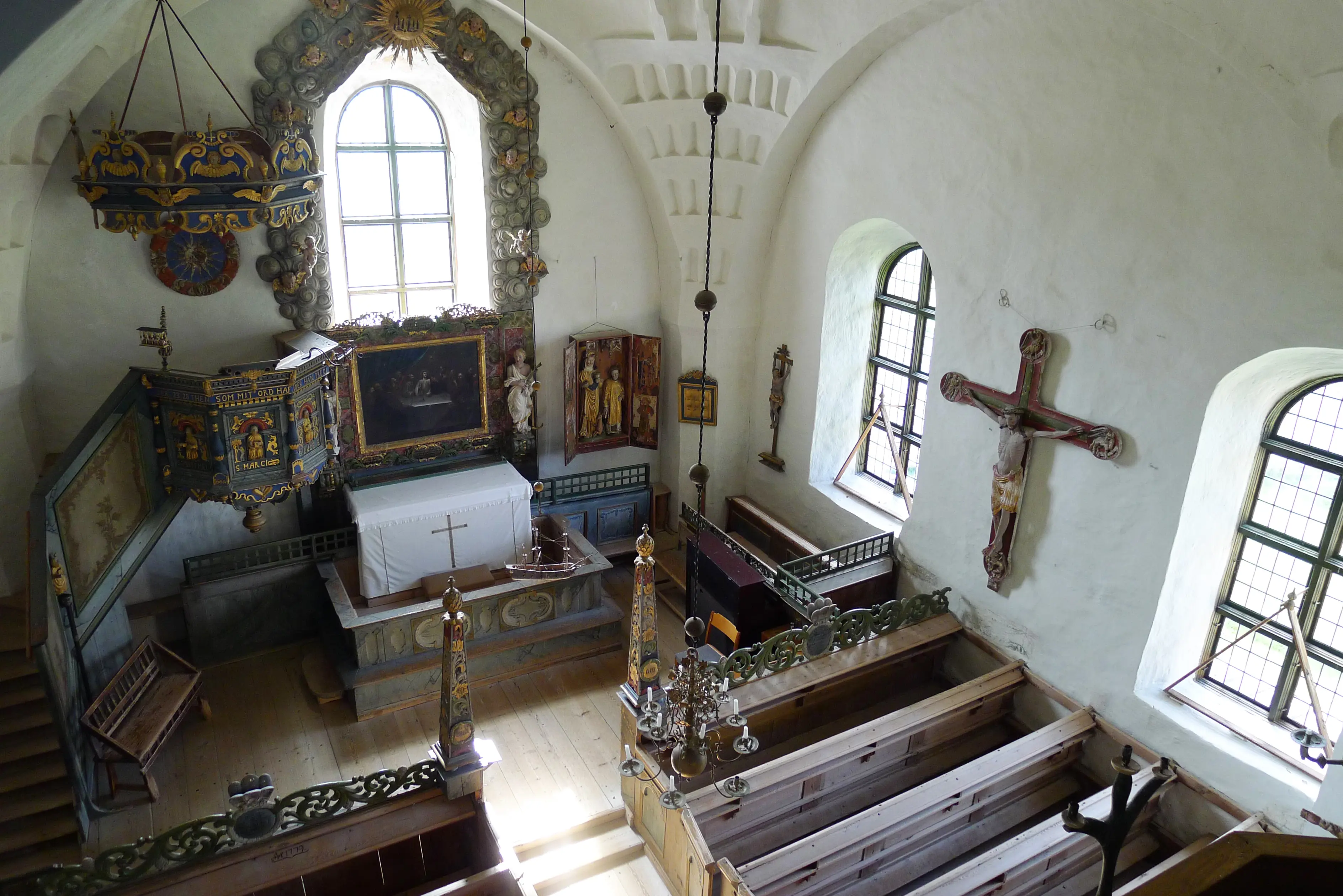 Trönö gamla kyrka. Koret, sett uppifrån läktaren, är utsmyckat med rikliga och färg-glada träsnider. På en långvägg hänger ett stort krucifix.