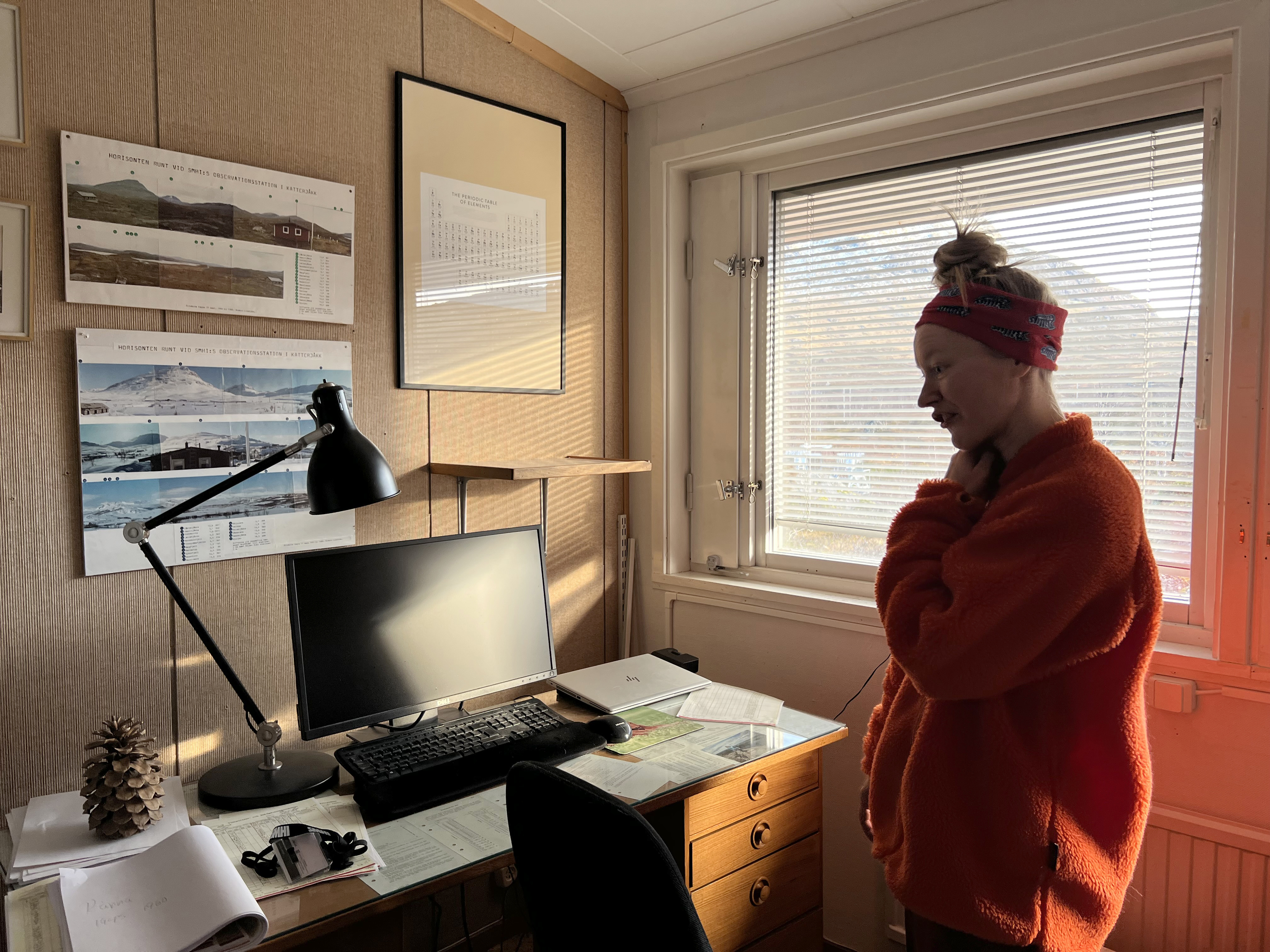 En person i orange fleecetröja står inne på sitt kontor. 