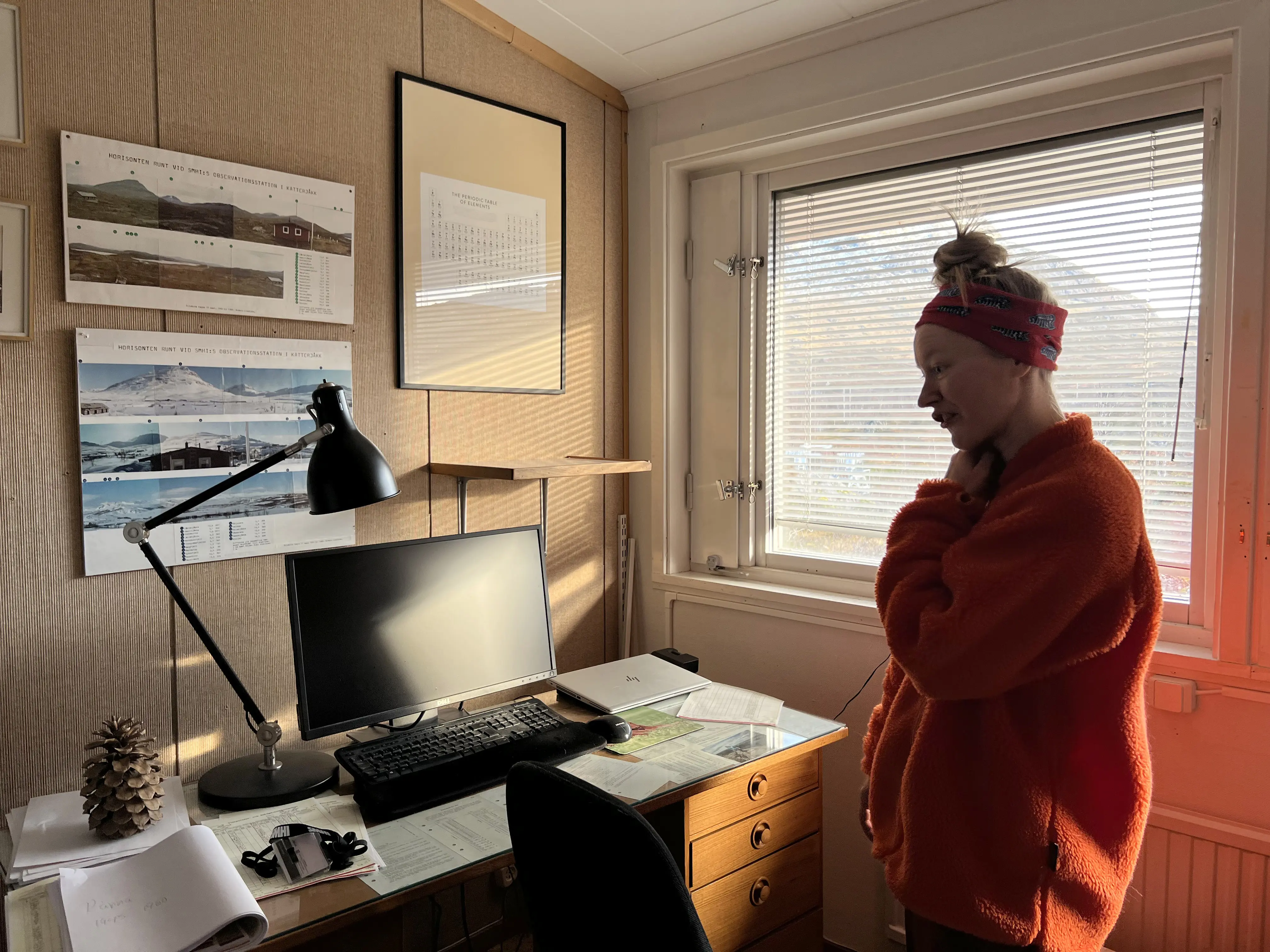 En person i orange fleecetröja står inne på sitt kontor.