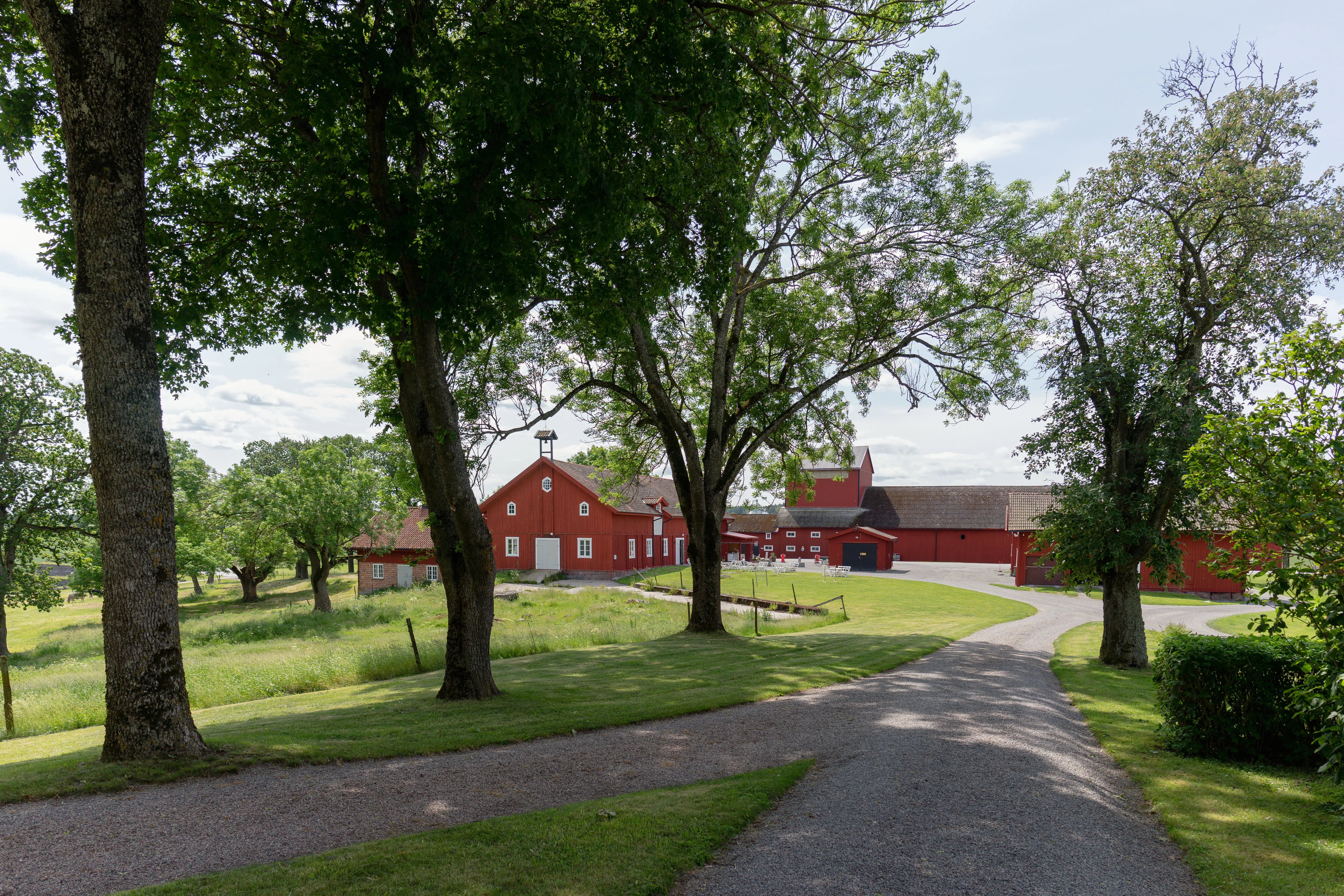 Landsberga. En bred grusgång leder ned mot en samling röda ekonomibyggnader.