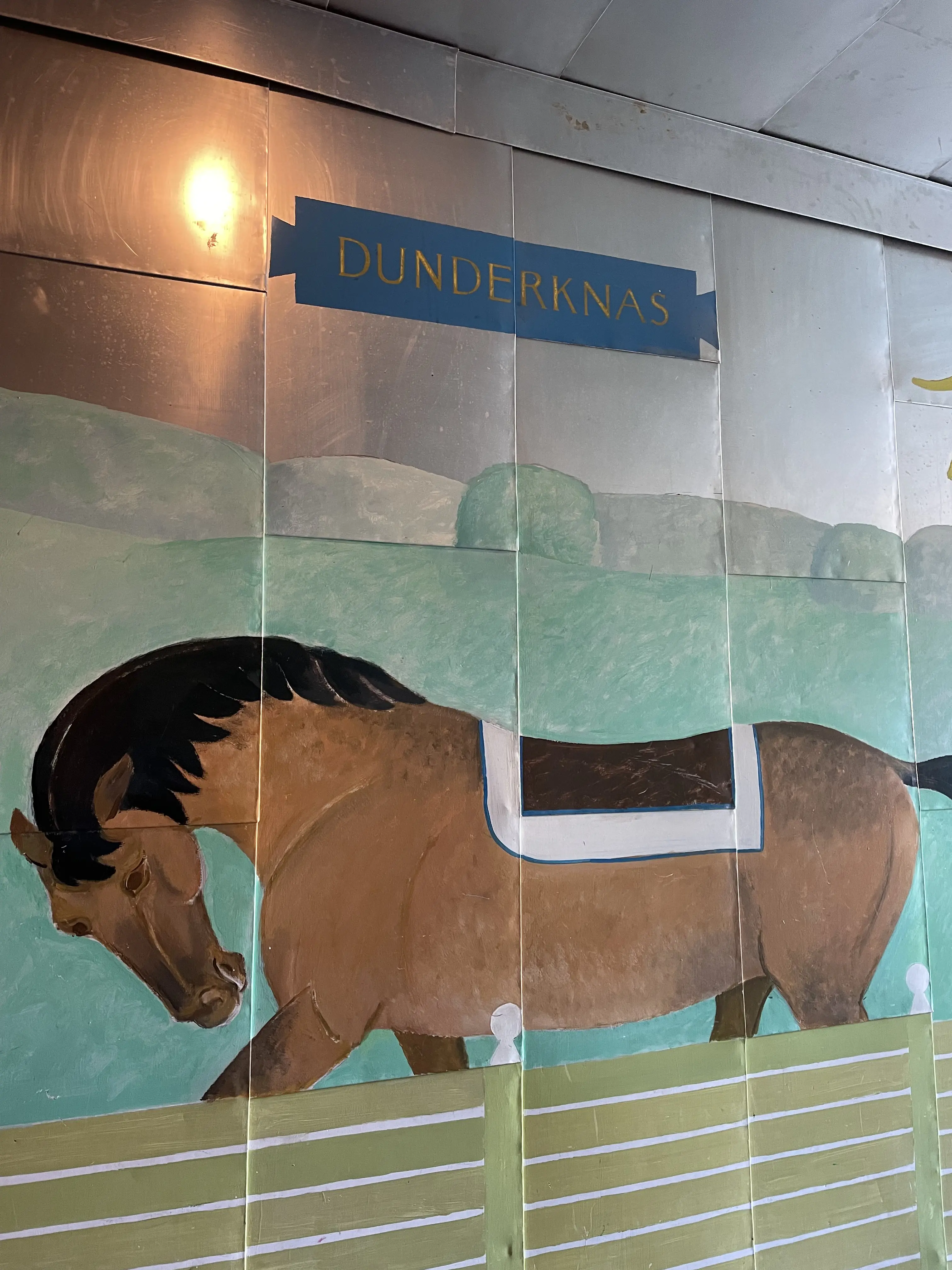 Mellersta koppartältet i Hagaparken. Gång till byggnadens baksida. På en plåtklädd vägg är en häst målad, med överskriften "Dunderknas".