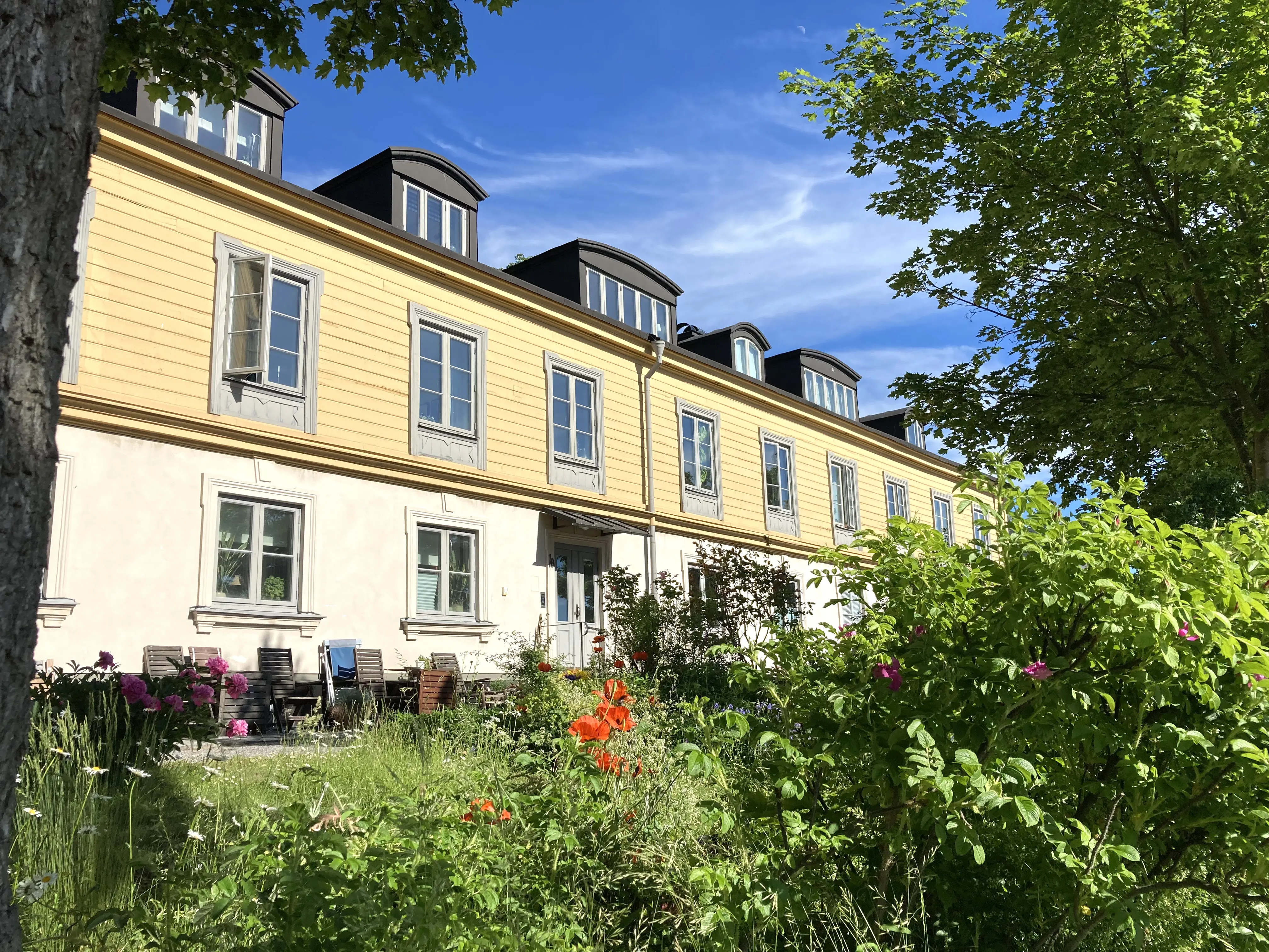 Hantverkarbostället, Kastellholmen. Tvåvåningsbyggnad med många tak-kupor. Fasaden är delvis vitputsad och delvis klädd i gult trä. Sommar, blommor och grönska.