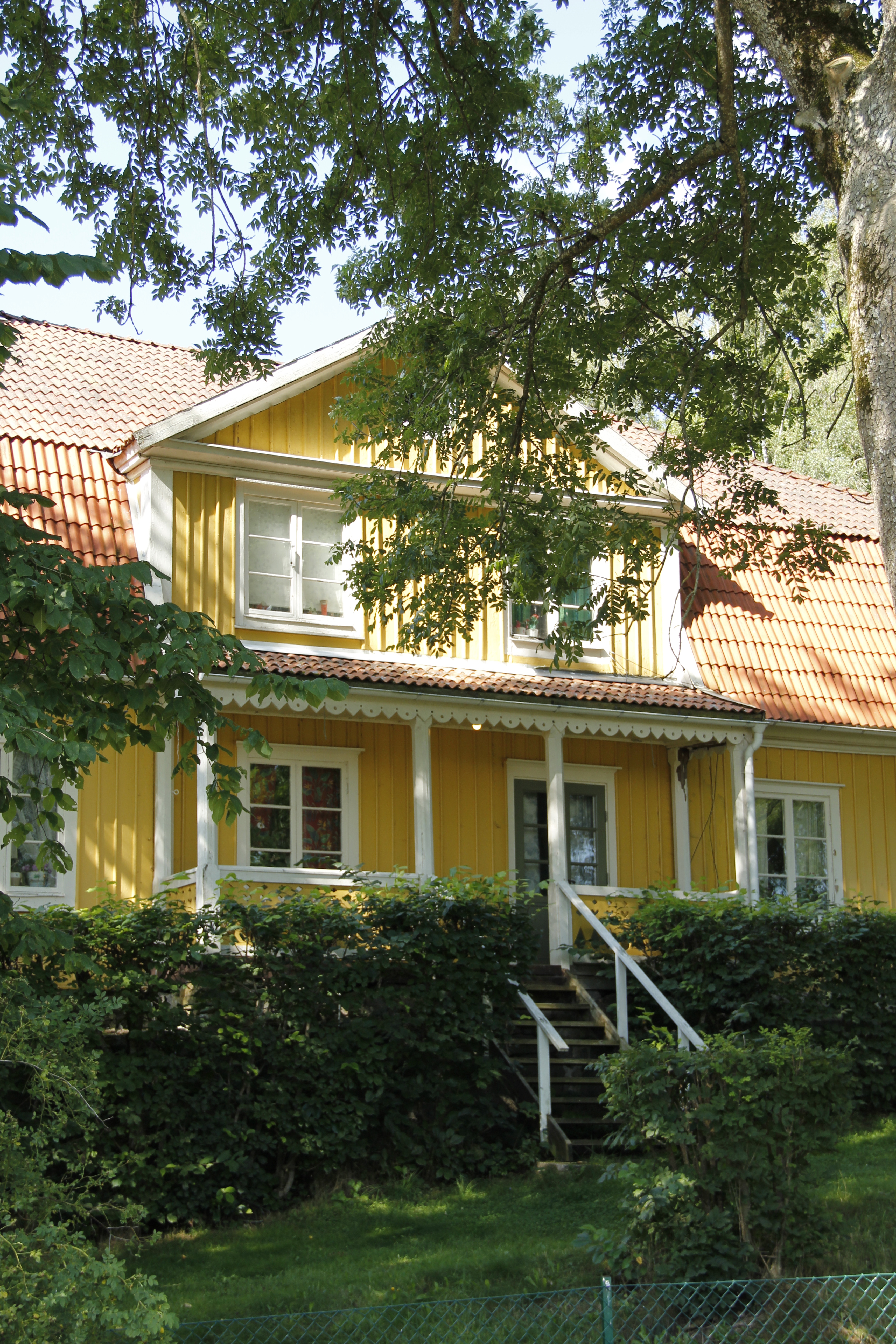 Arrendatorbostaden vid Huseby kronoegendom. En gul trävilla med vita snickerier och brutet tegeltak. Sommar och grönska.