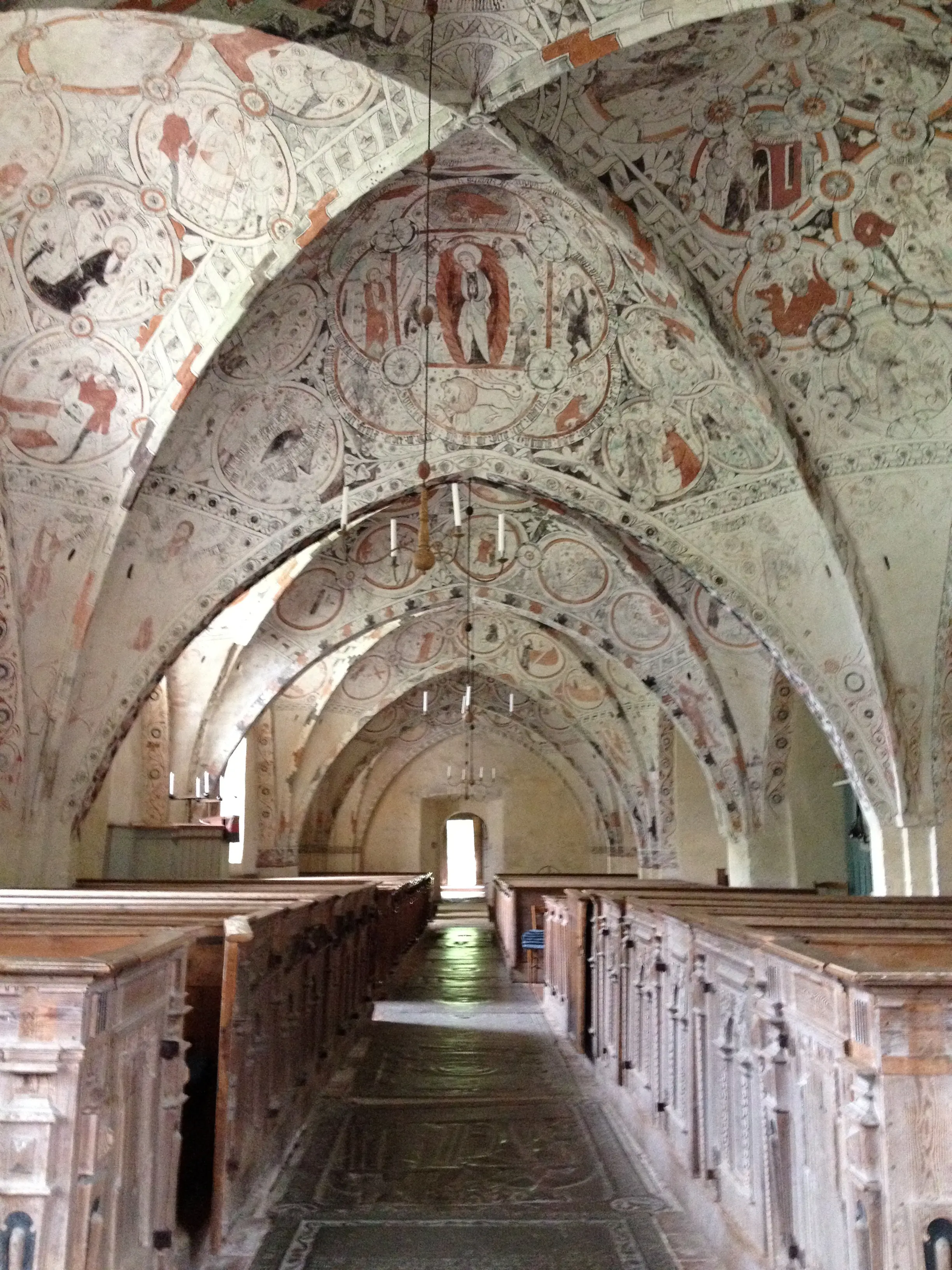 Interiör, Risinge gamla kyrka. Medeltida kryssvalv med målningar. Kyrkbänkarna är av vackert snidat trä. Mittgången utgörs av gravhällar.