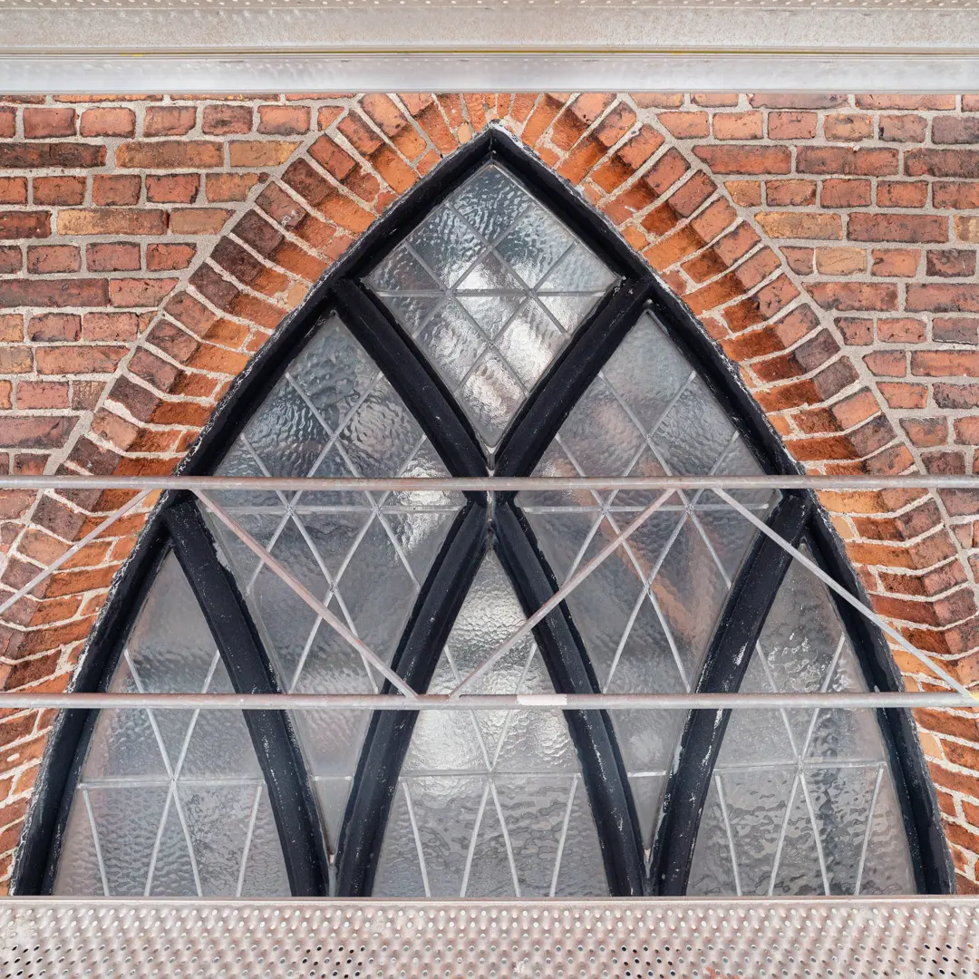 Spetsigt fönster i röd tegelvägg, delvis skymt av metallräcken