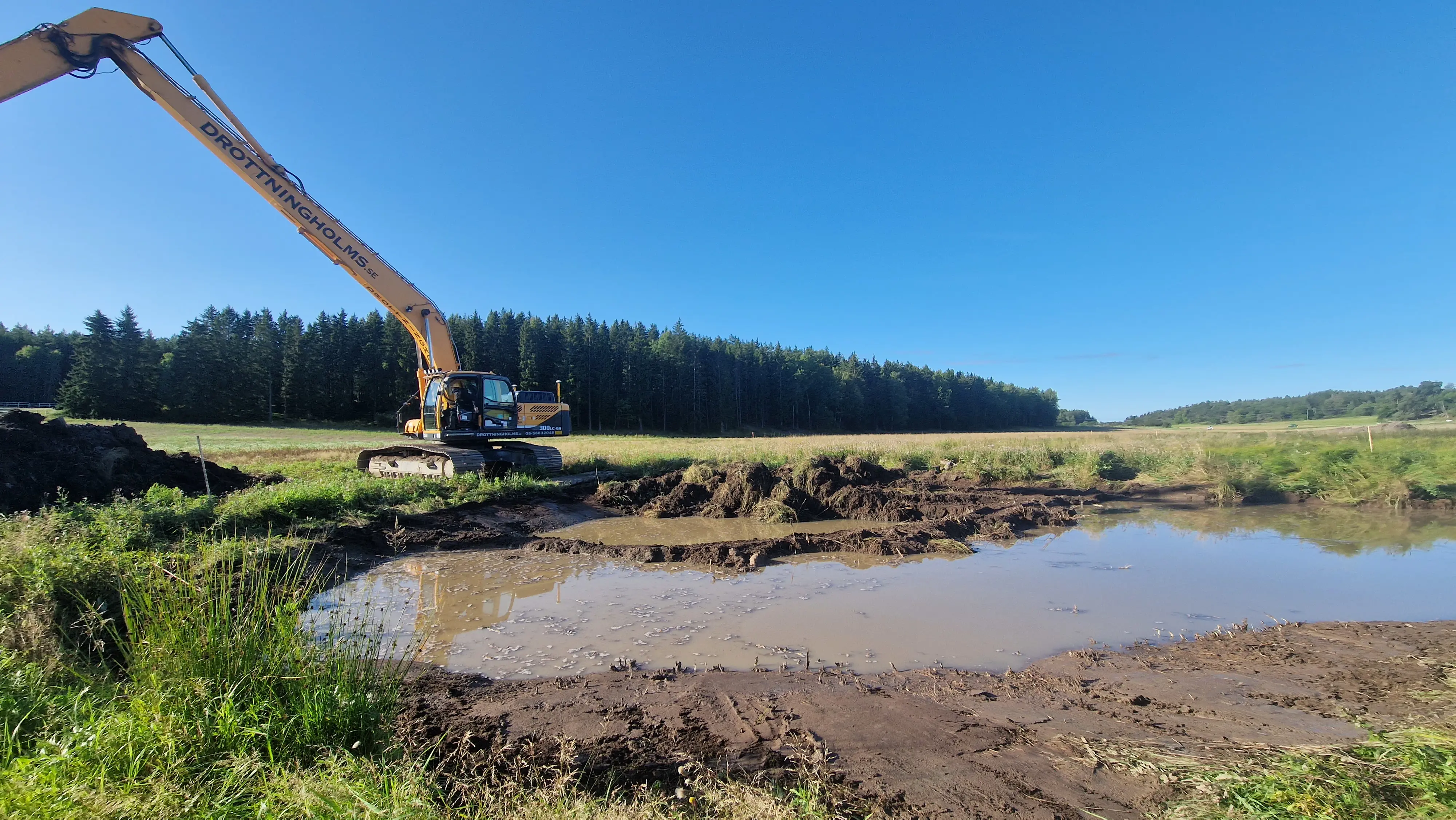 Jordbrukslandskap där en grävare skapar en sänka för återvätning av våtmark.
