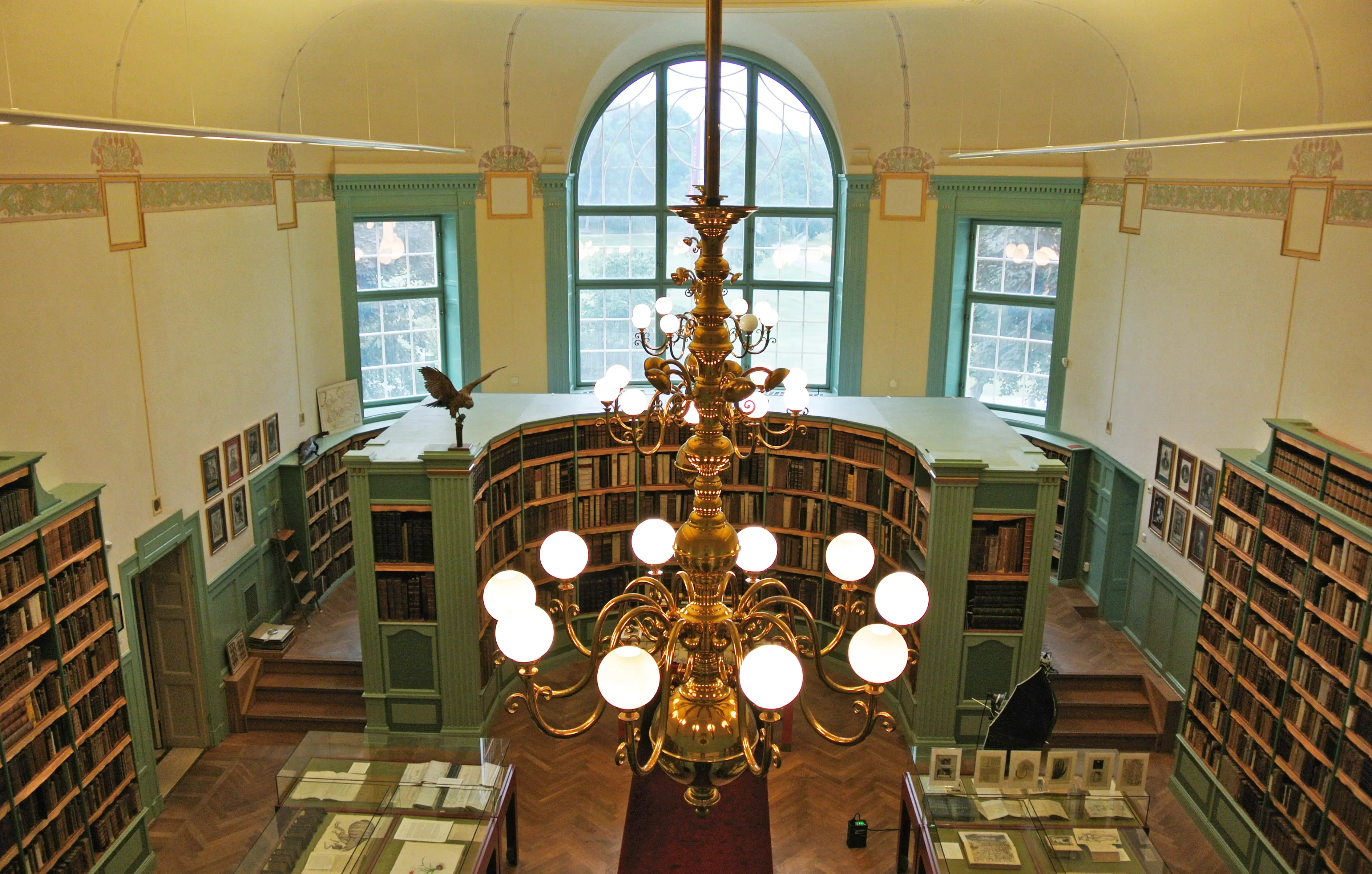 Hagströmerbiblioteket i Haga tingshus, med bokhyllor och montrar. Tak och väggar är ljusgula, inredningen är grön. Trägolvet är fiskbensmönstrat.