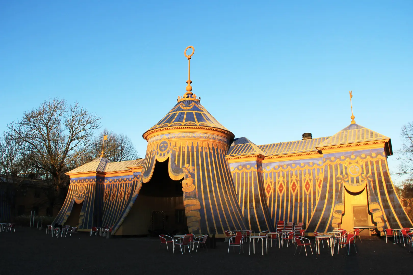 Koppartälten i kvällsljus med kafébord och stolar framför.