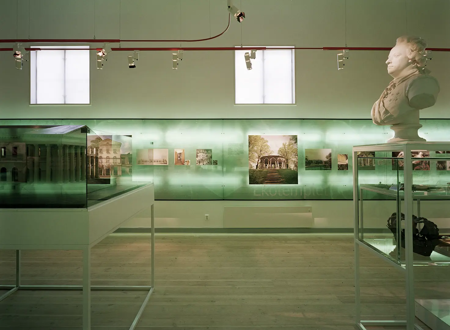 Interiör från Haga parkmuseum med fotografier på väggen, glasmontrar med föremål och en byst.