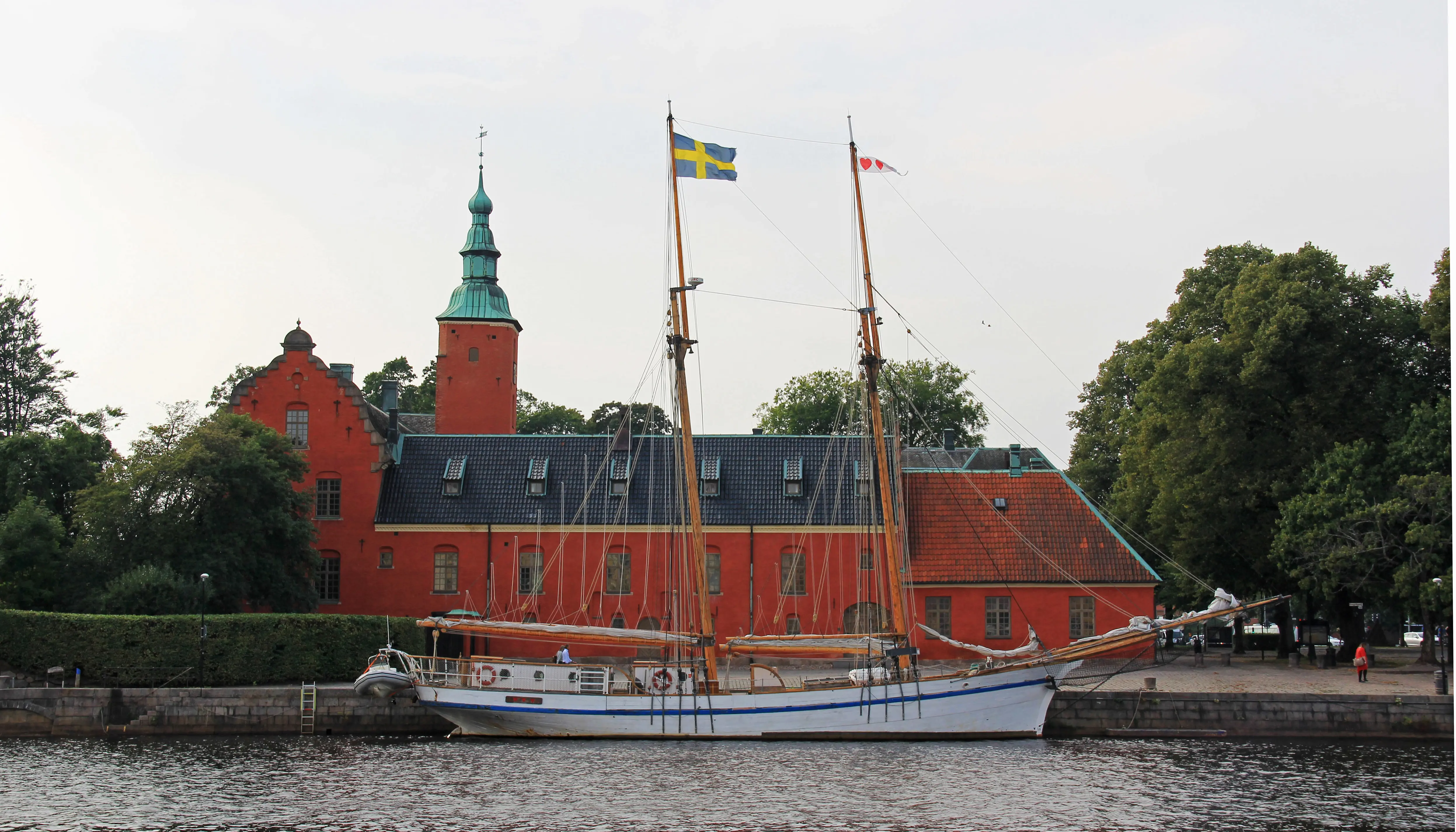 Halmstads slott sett över vattnet. Vid kajen framför slottet ligger ett tvåmastat skepp.