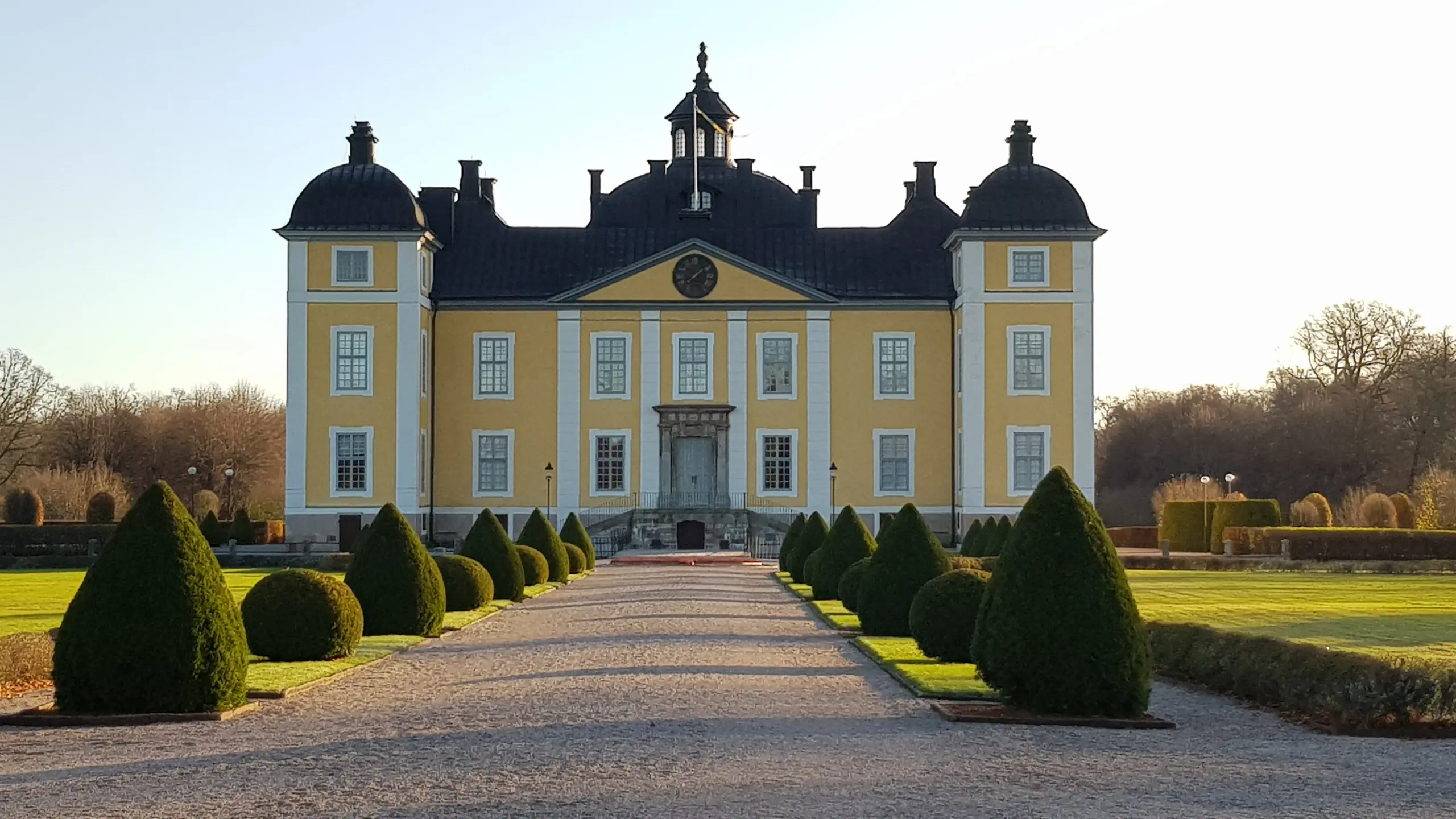 En allé som leder till en gul slottsfasad