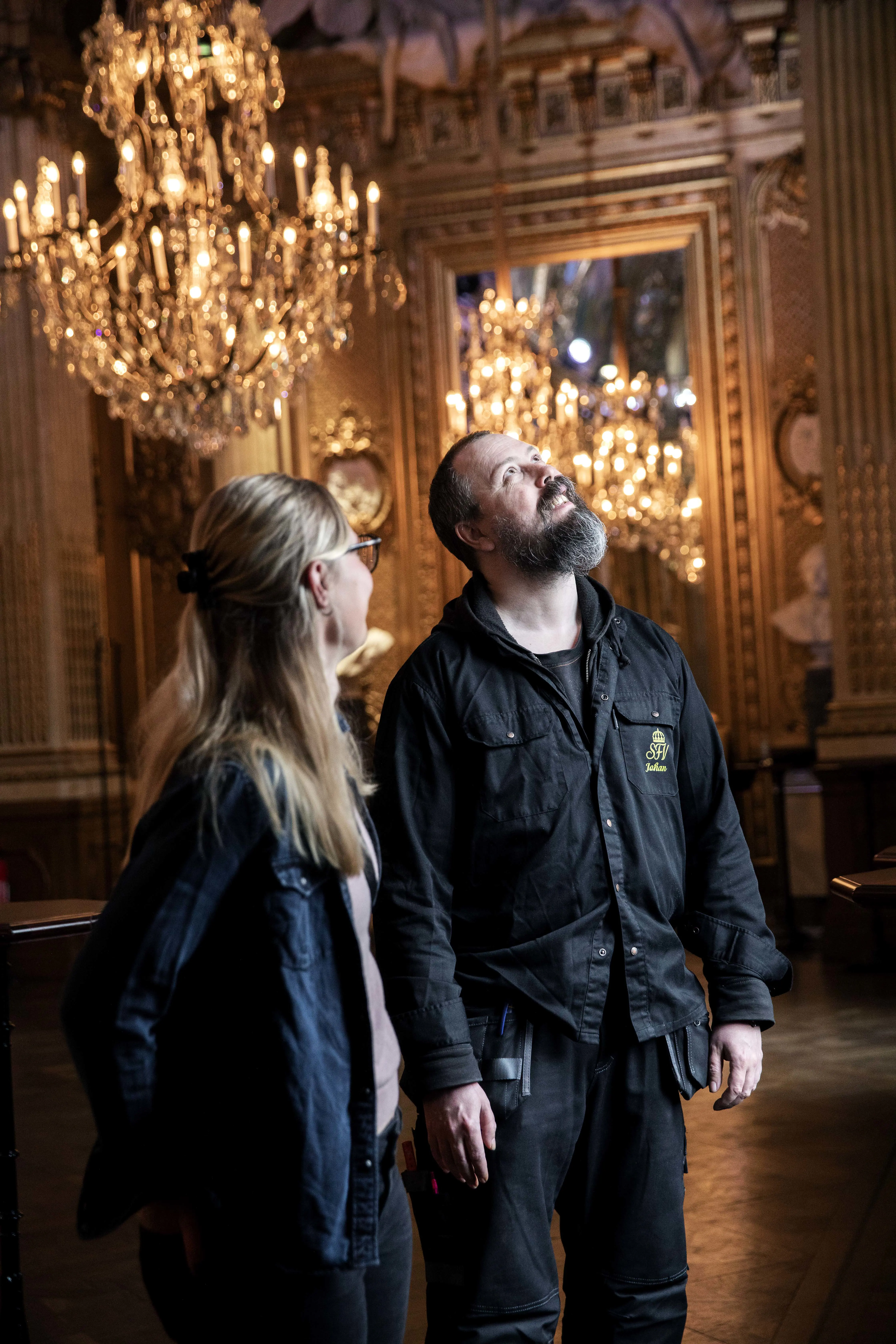 Två personer tittar upp mot taket i ett rum med kristallkronor.