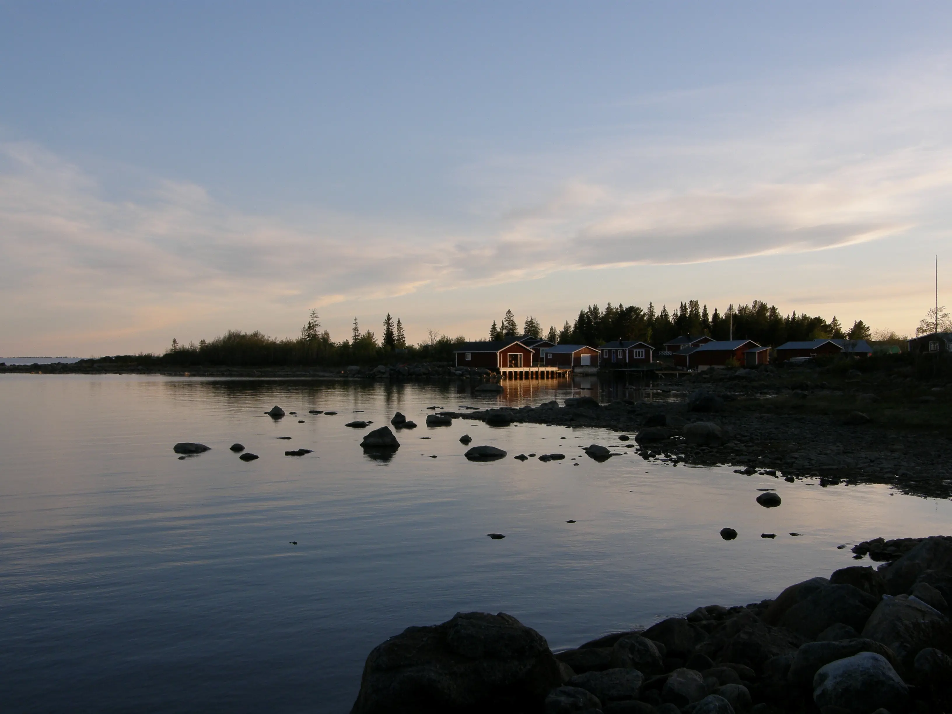 Fiskeläge på Kluntarna, inramat av barrskog och vatten. Sommarkväll.