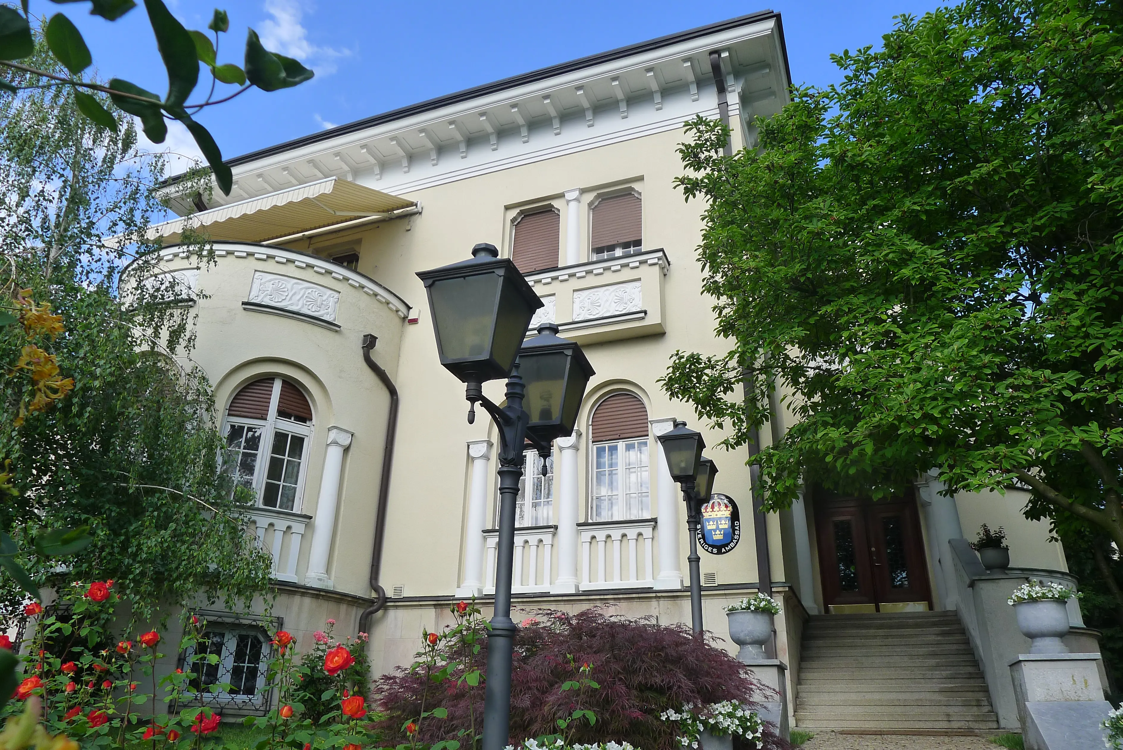 Ambassaden i Belgrad. En klassicistisk villa i gräddvit puts, inramad av lummig växtlighet.