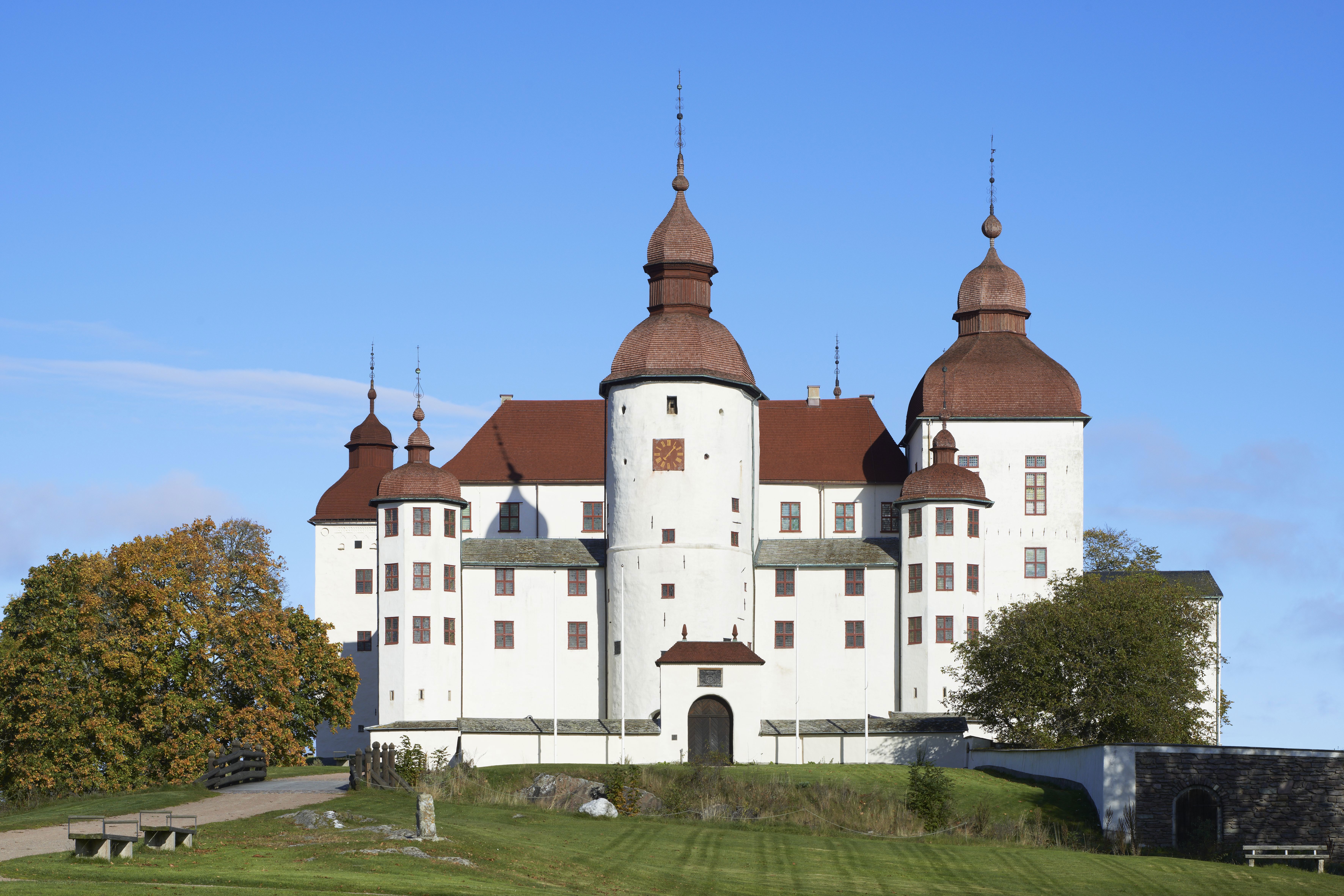 Läckö slott. Vitputsad, borgliknande byggnad med flera torn i olika form och höjd. Tornen kröns av spånklädda lök-kupoler.