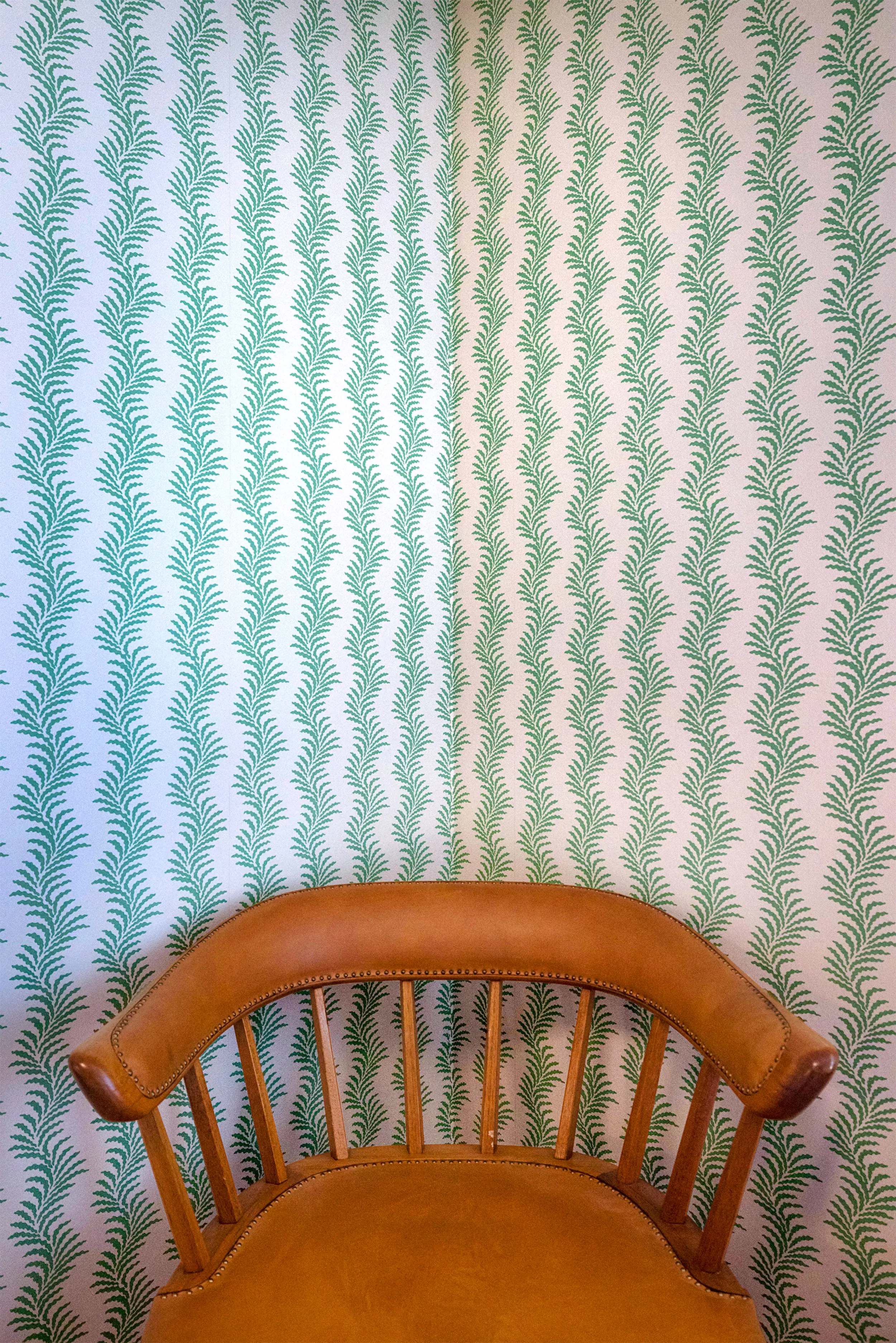 Tapet med gröna mönsterslingor av ormbunkar. Framför tapeten står en läderklädd stol.