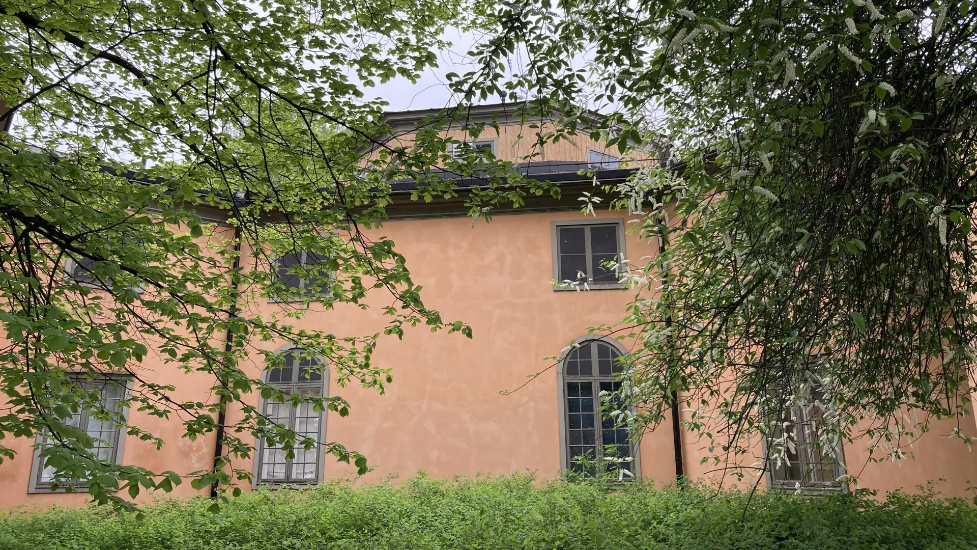 Västra koppartältet. En varmgul byggnad i två våningar, inbäddad i lummig grönska.