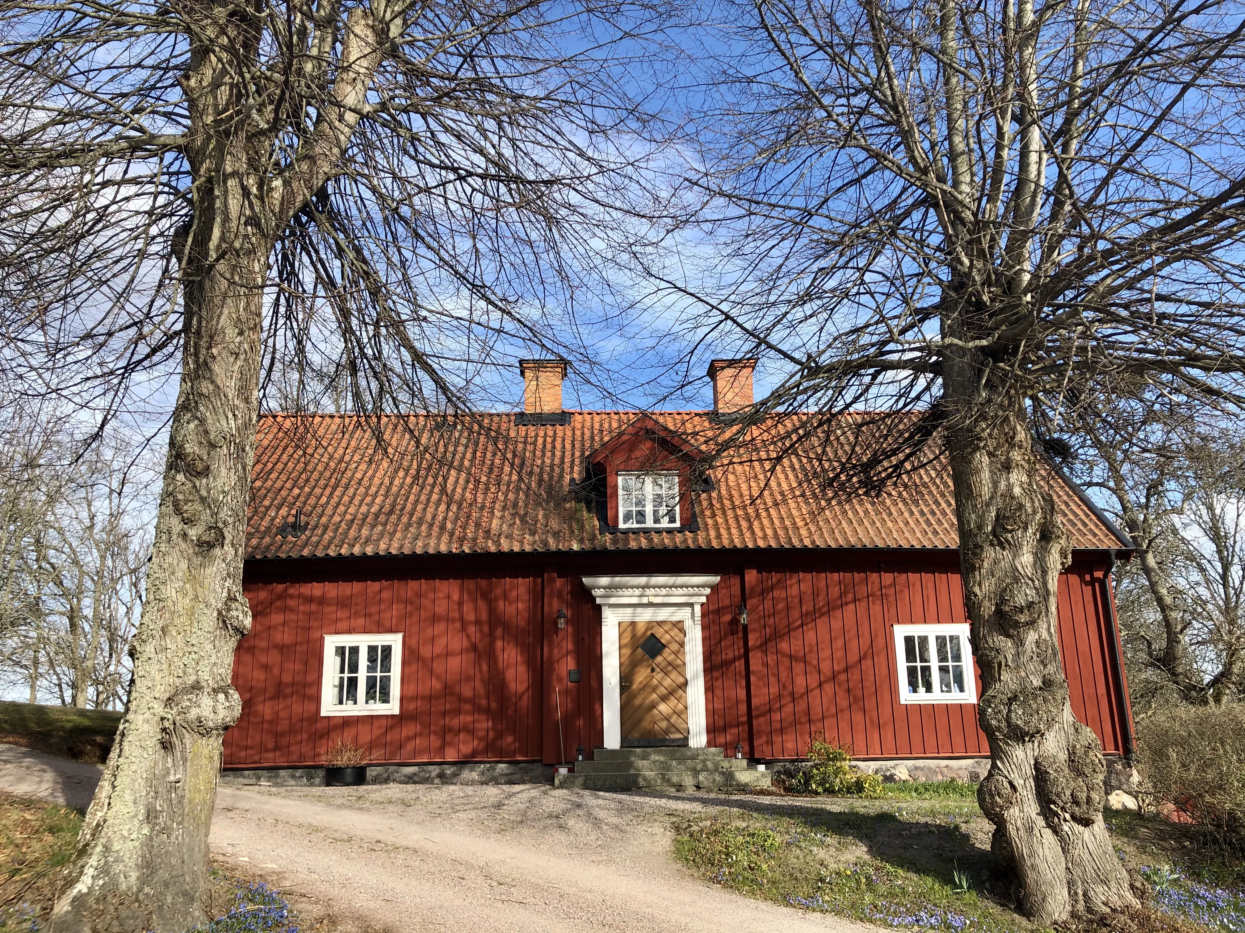 Tidigare mangårdsbyggnad på Stora kungsladugården. Röd byggnad med tegeltak och två skorstenar. Tidig vår.