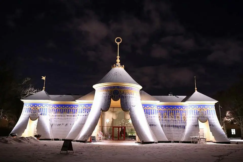 Mellersta koppartältet i Hagaparken. Fasaden är belyst nedifrån. Dess blåa och gula färger skymtar under ett tunt snötäcke. Kväll.