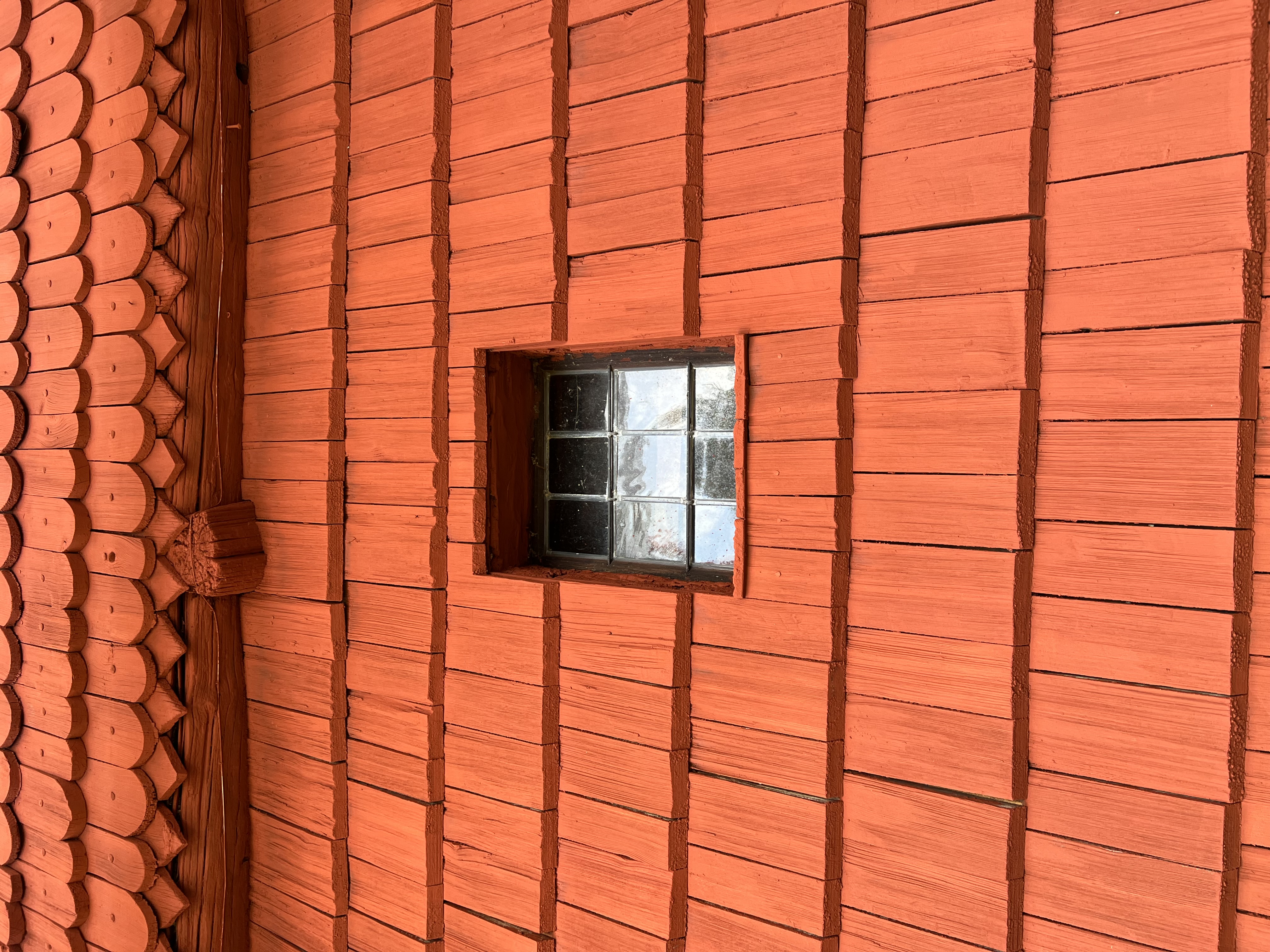 Ornäs-stugan. En del av den spånklädda fasaden, målad i Falu ljusröd, med ett litet blyinfattat fönster.