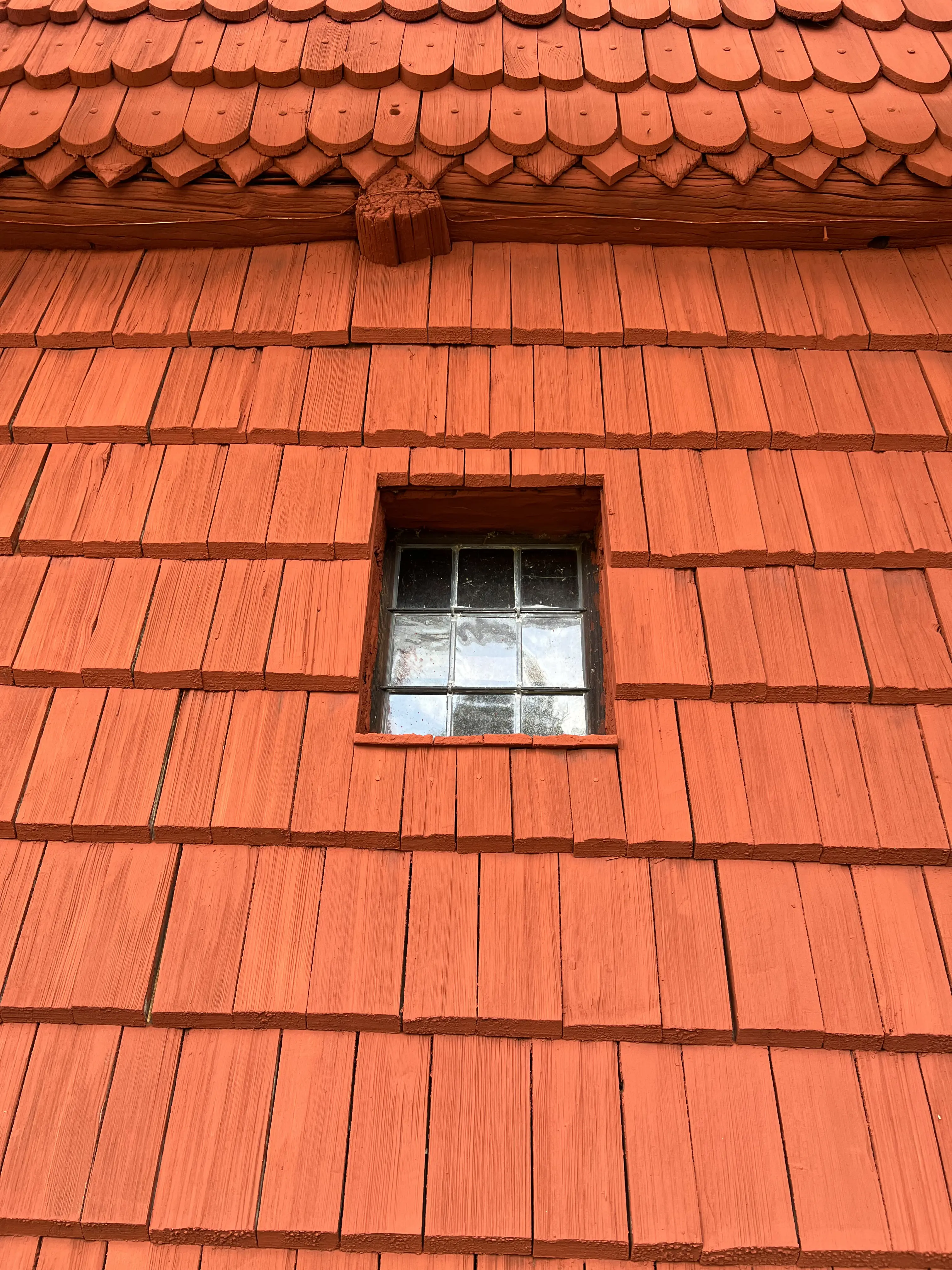 Ornäs-stugan. En del av den spånklädda fasaden, målad i Falu ljusröd, med ett litet blyinfattat fönster.