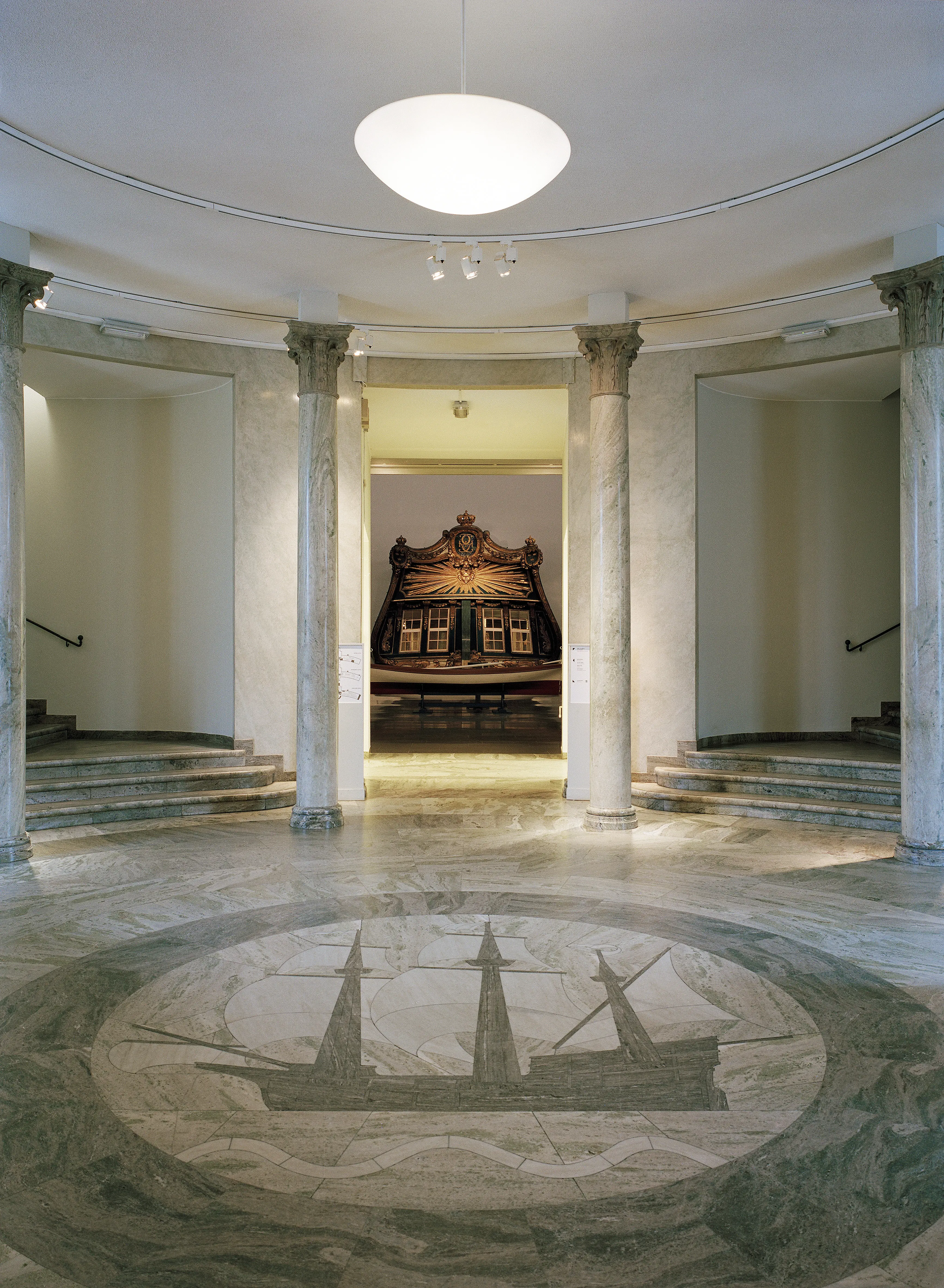 Sjöhistoriska museet, rotundan. Marmorgolvets skepps-motiv ramas in av pelare. Genom en dörröppning syns utställningsföremål.