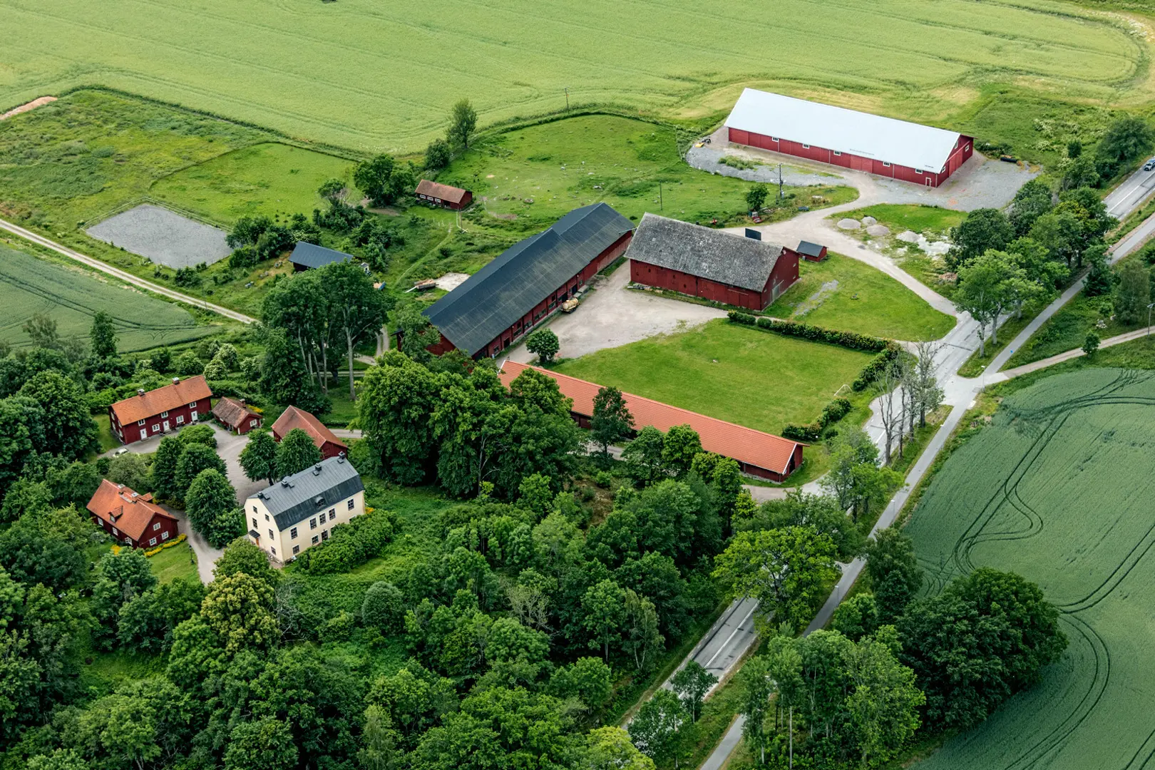 Flygbild av stora kungsladugården som omges av lövträd och gröna åkrar.