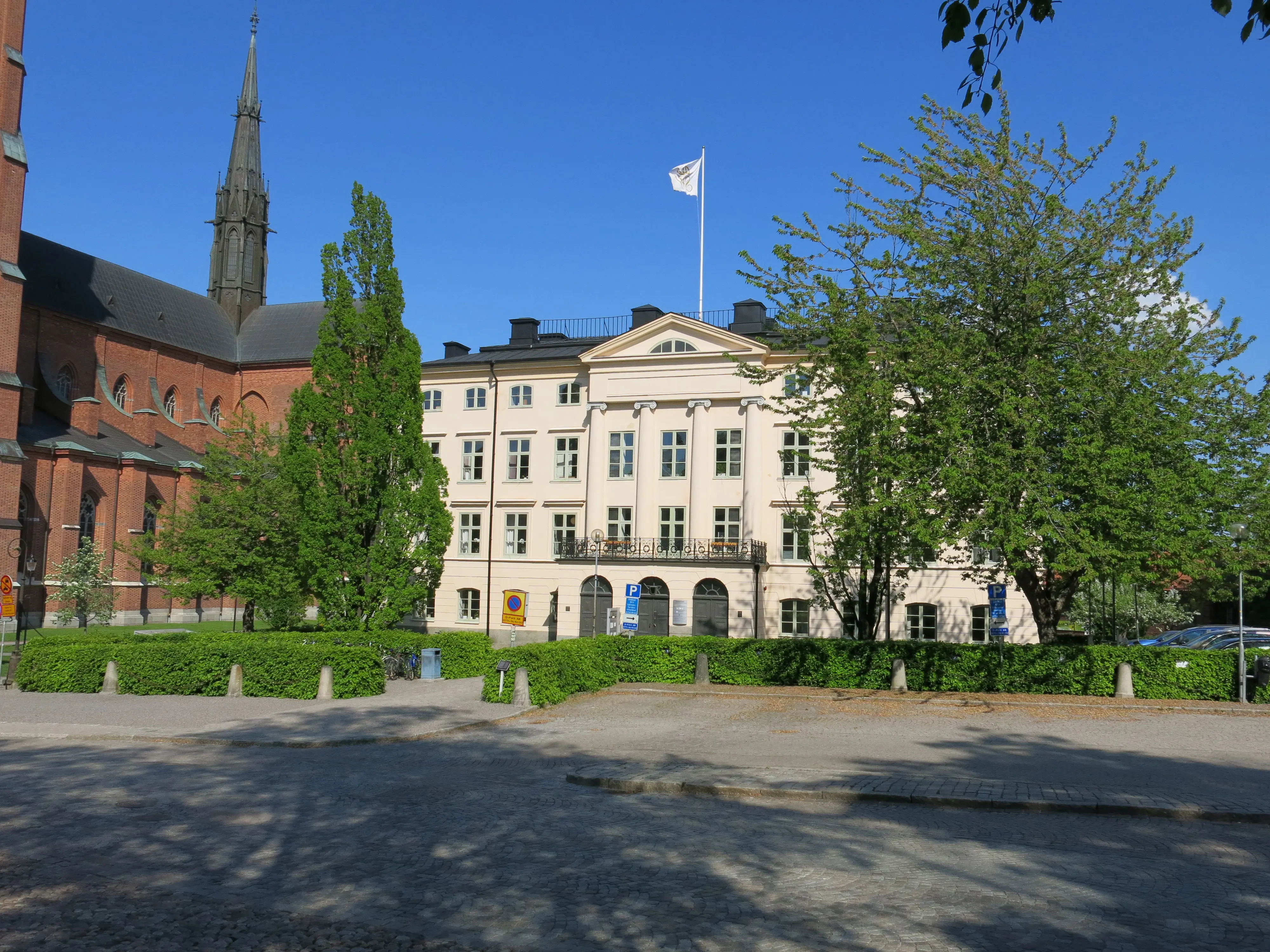 Dekanhuset, Uppsala. En vit, klassicistisk fyravåningsbyggnad intill domkyrkan. Vår och grönska.
