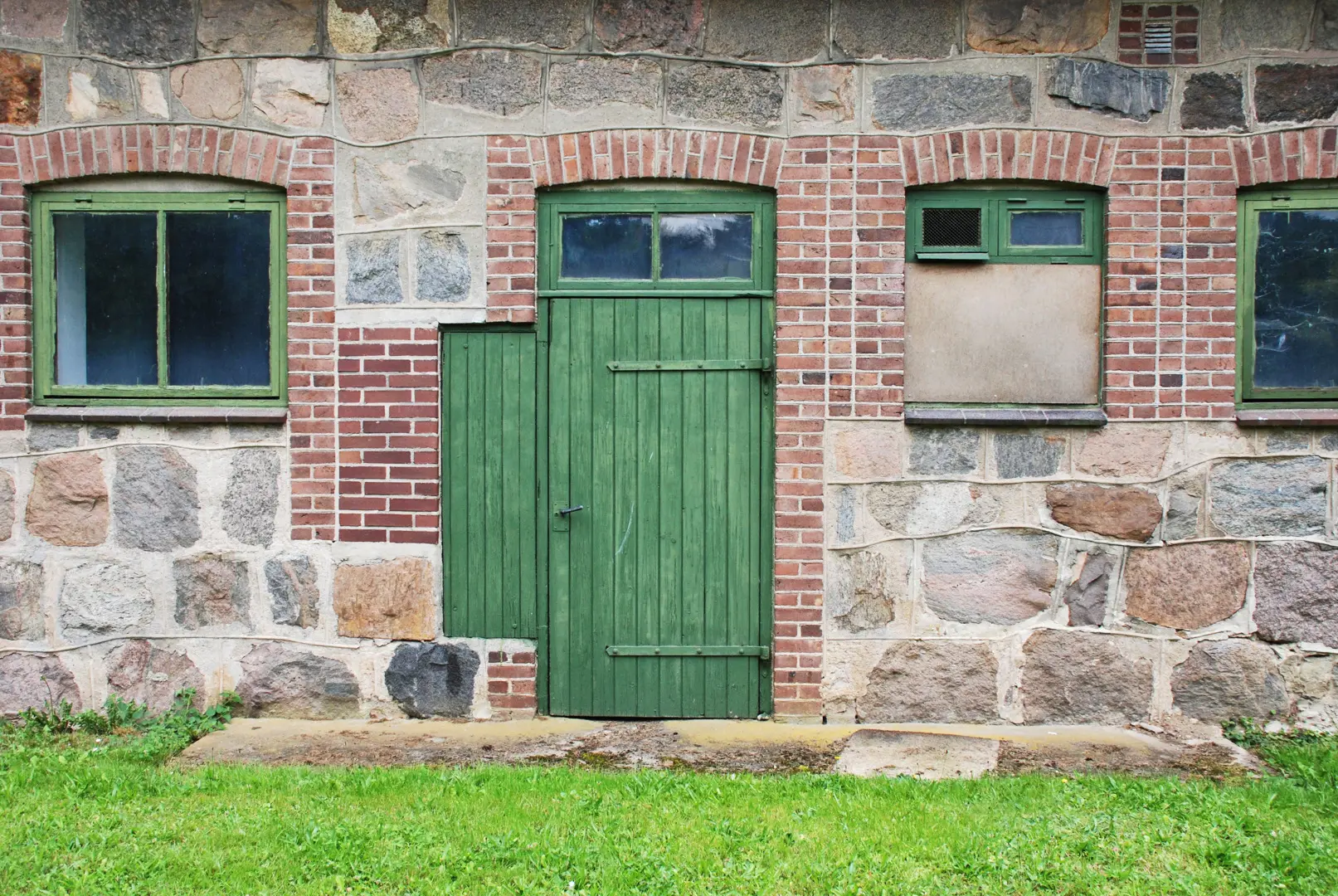 Grön trädörr i en ladugårdsbyggnad med fasad av sten och tegelstenar.