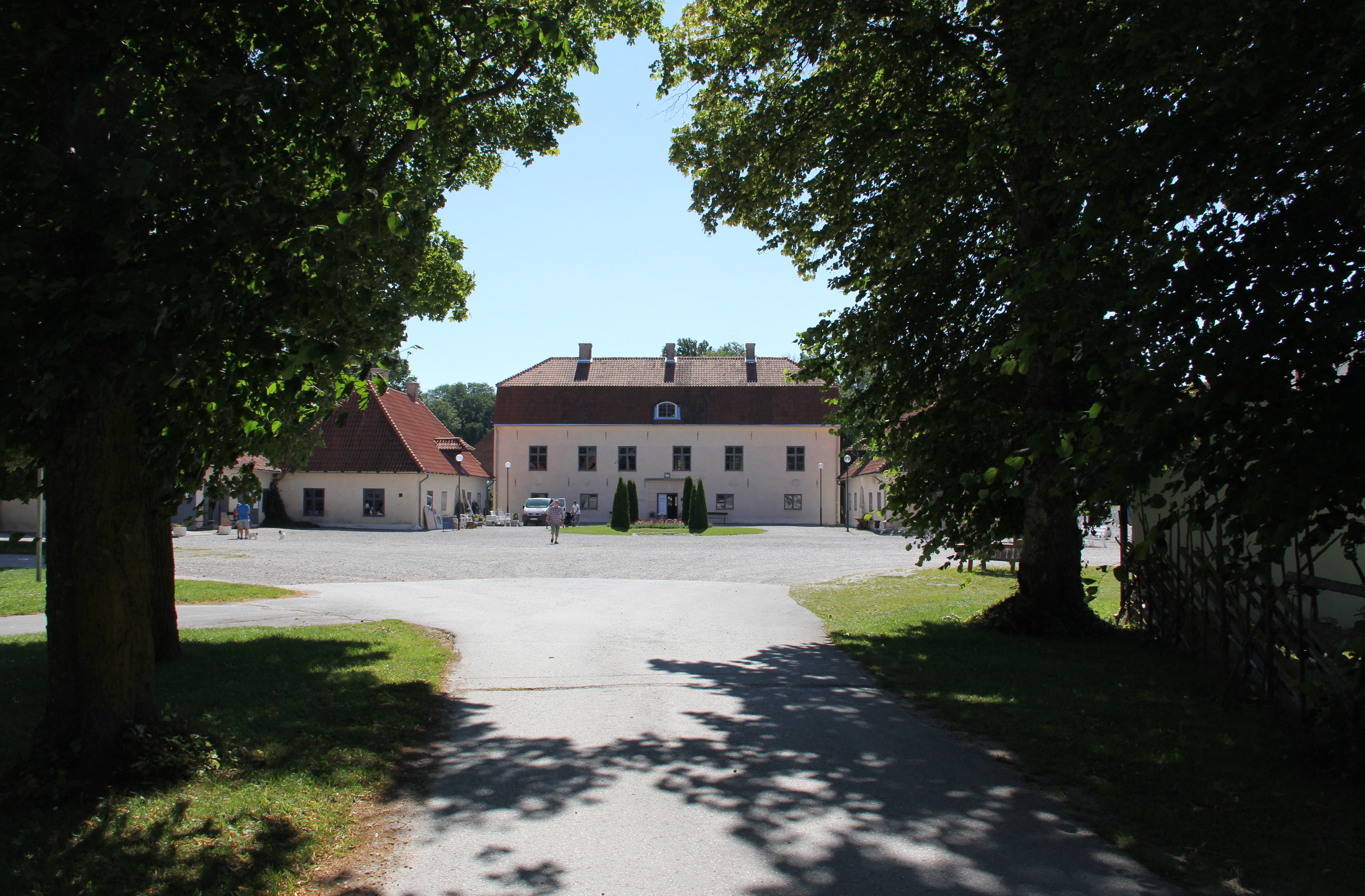 Roma kungsgård, en ljus ståtlig herrgårdsbyggnad med rött tak. En asfalterad väg, med träd på sidorna, som leder fram mot byggnaden.